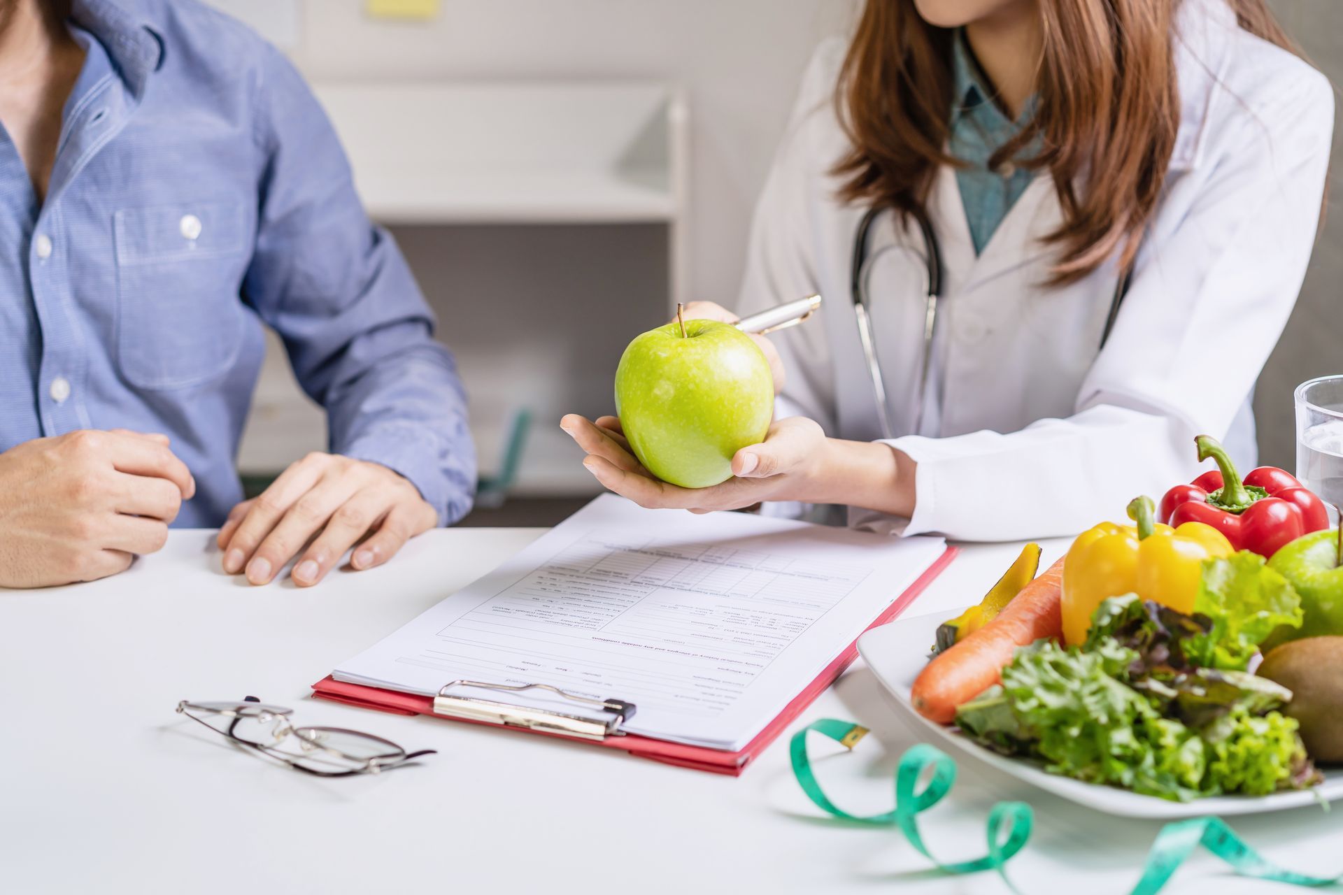 Dietitian consults with a patient, holding an apple, with fresh produce on the table.