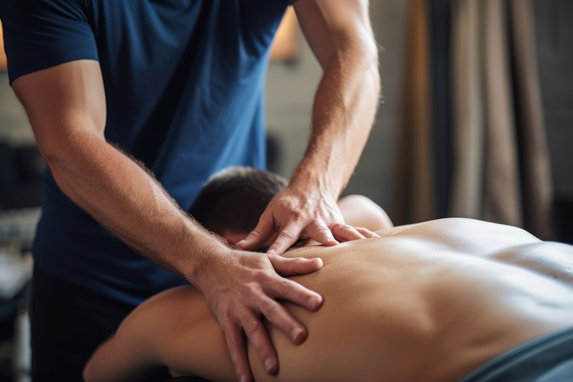 A man receiving a massage. A therapist's hands on his back, blue shirt, light setting.