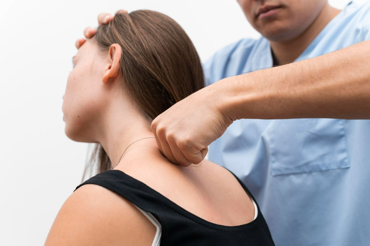 A healthcare provider adjusting a patient's neck. The patient is a woman in a black tank top.