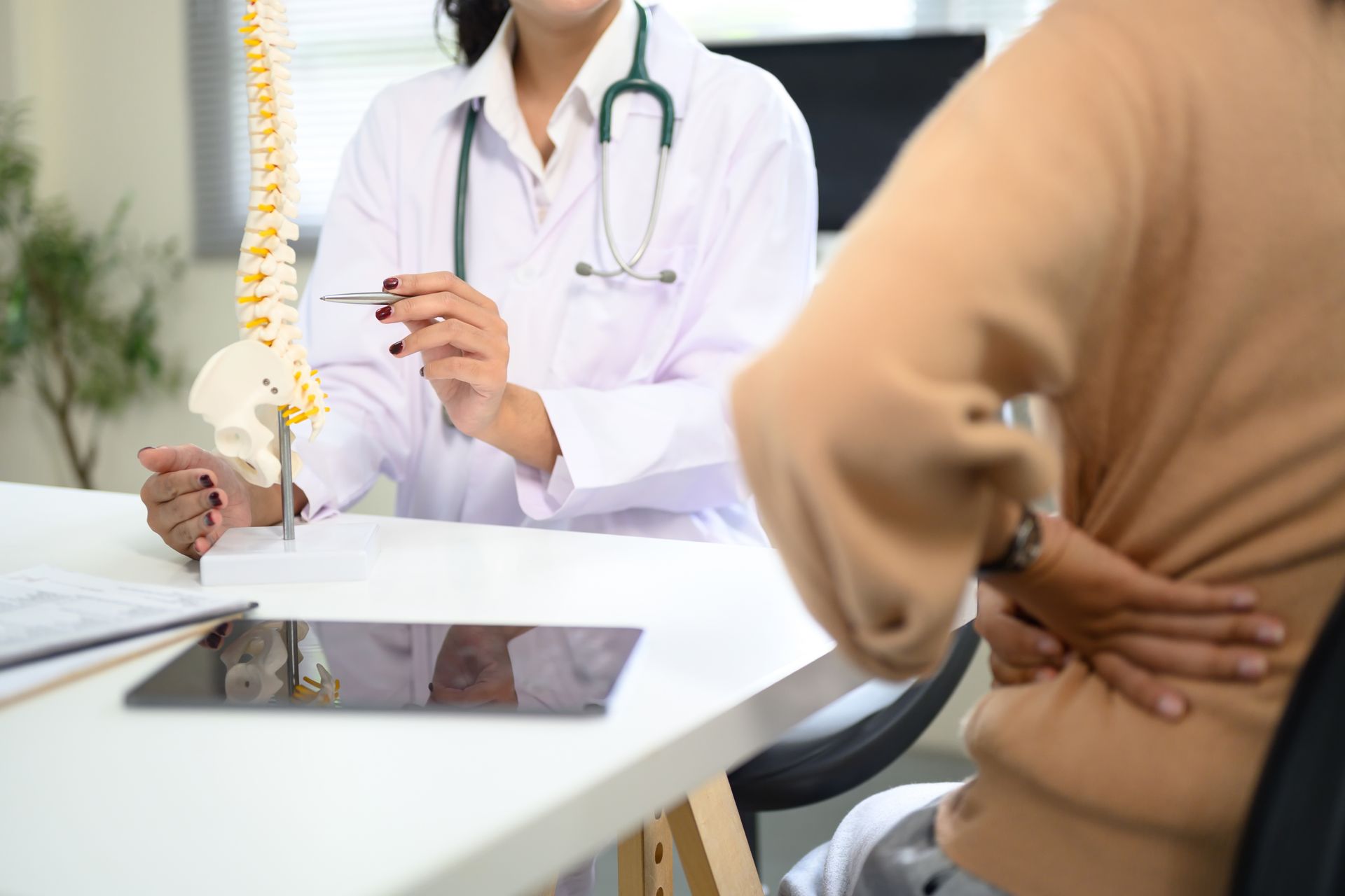 Doctor explaining spine model to patient with back pain.