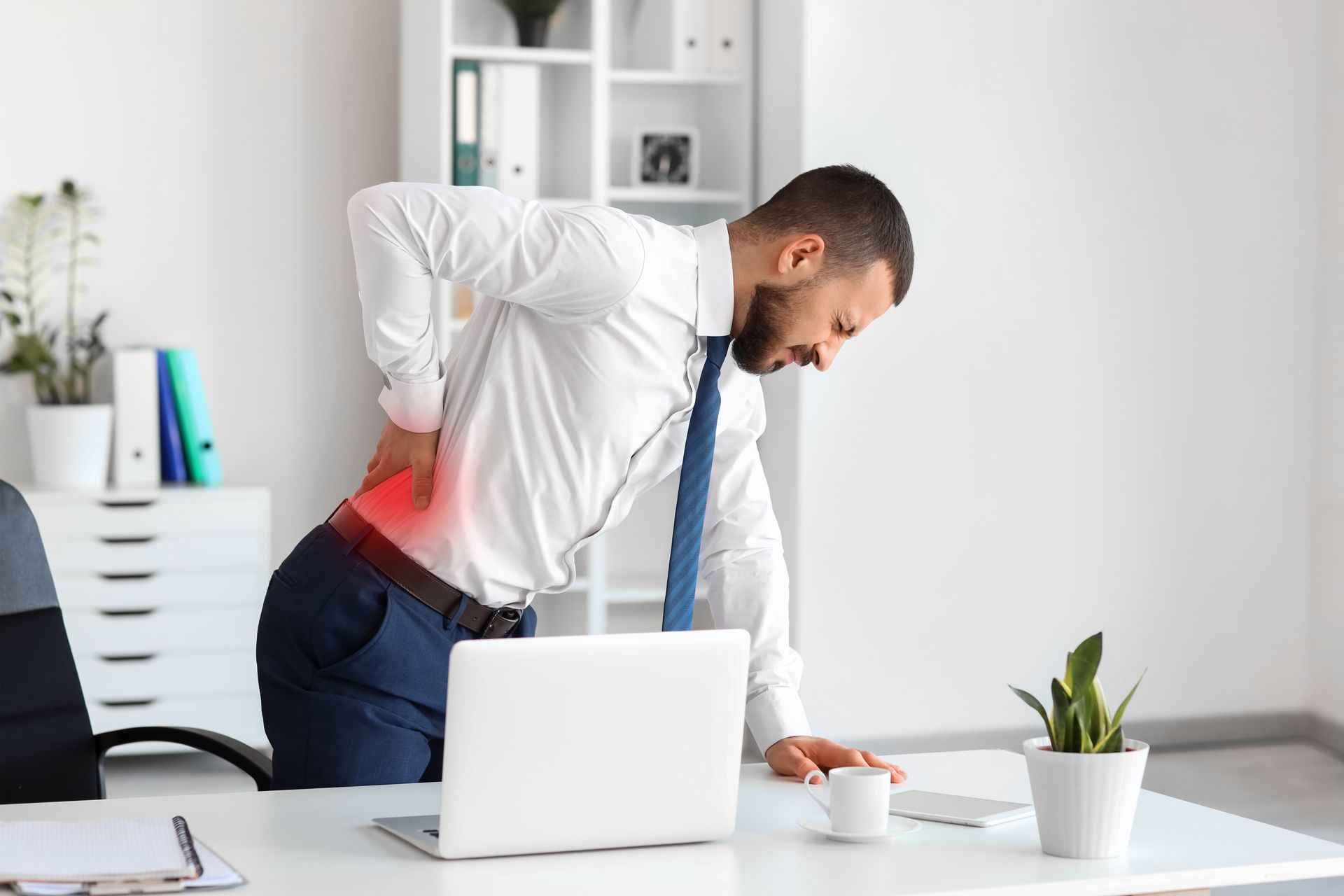 Man in office shirt bent over, touching back near red highlight, appearing in pain.