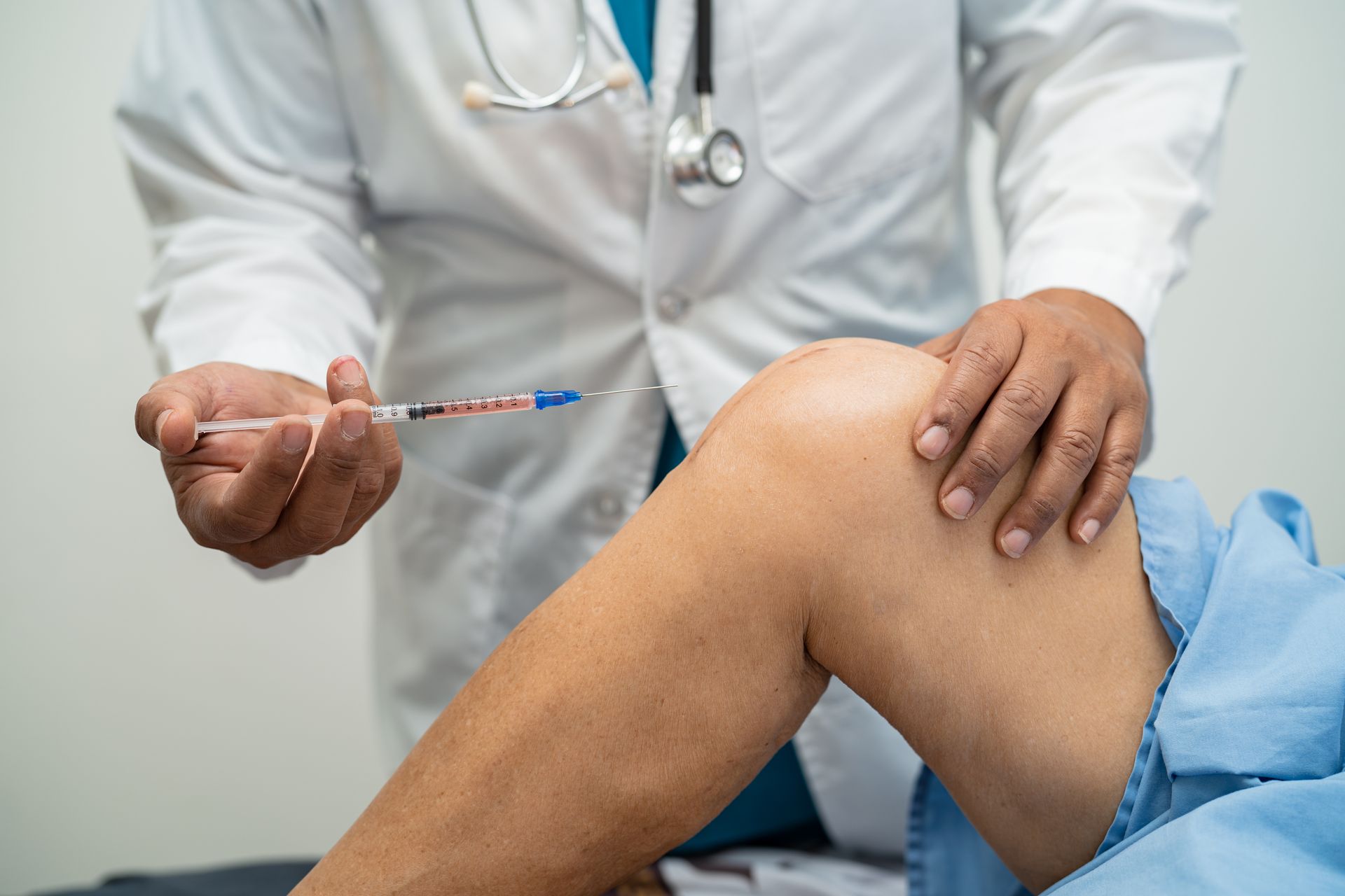 A doctor is giving an injection to a patient 's knee.
