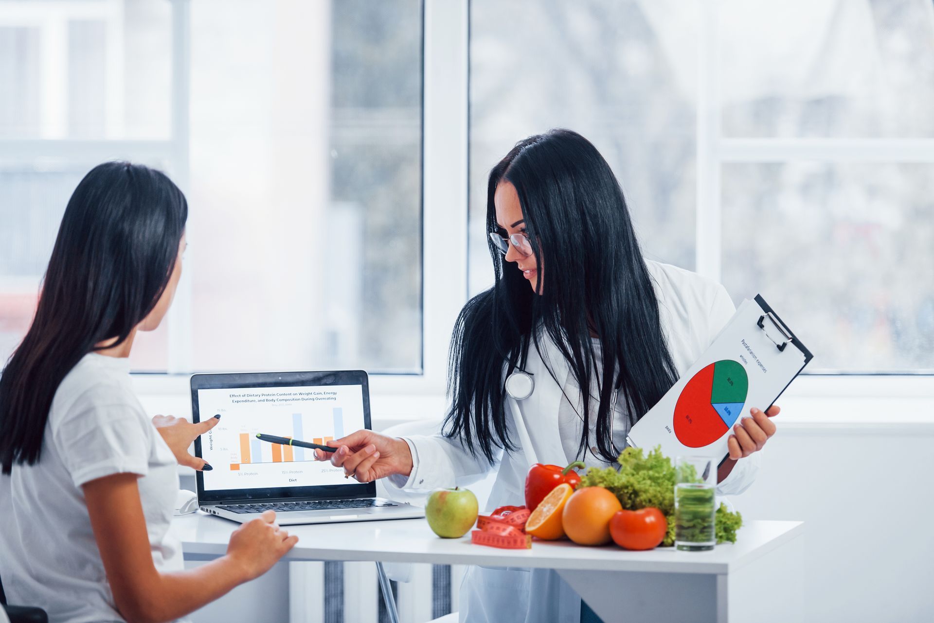 a nutritionist is talking to a patient at a table with fruit and vegetables .