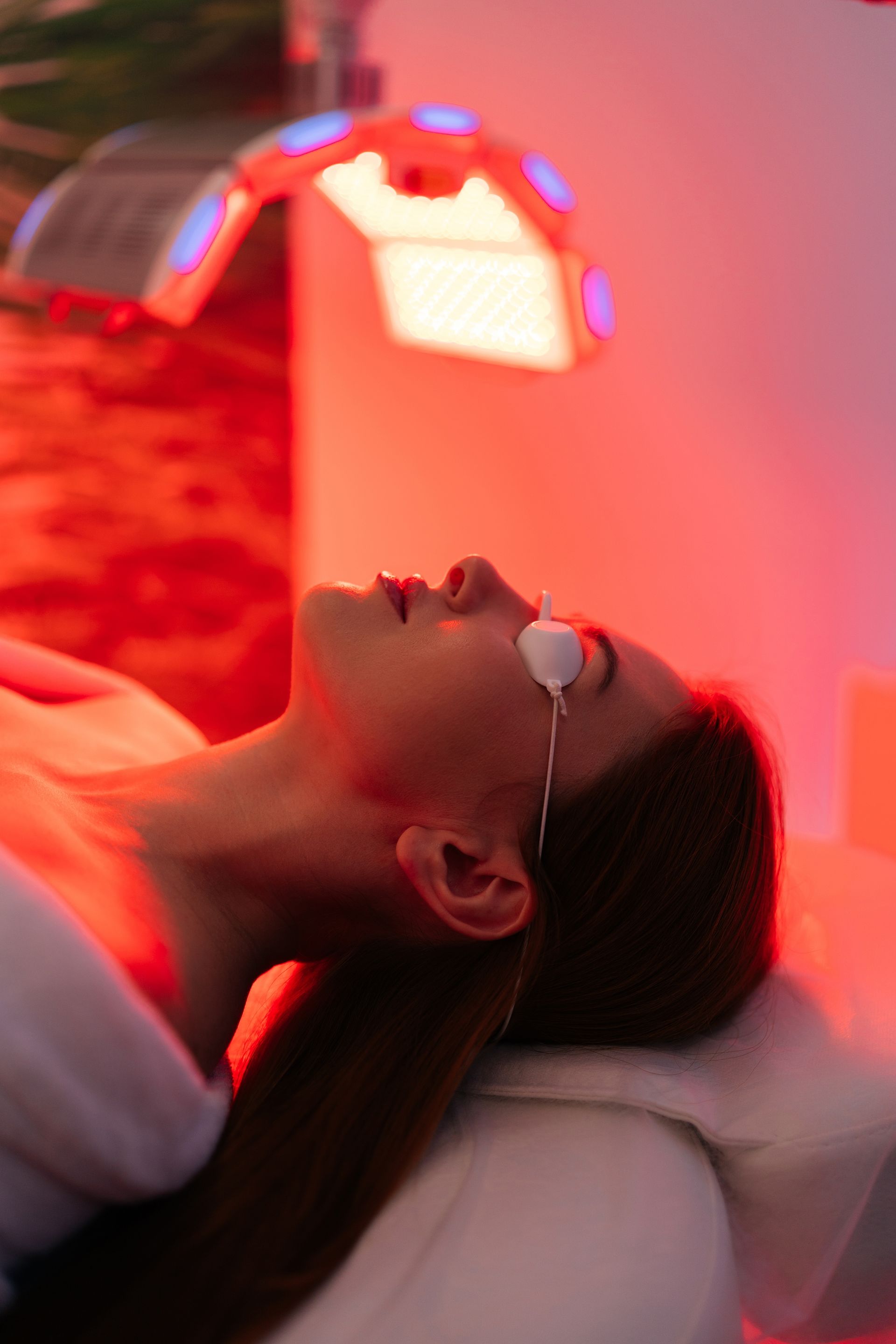 Woman receiving red light therapy, wearing eye protection, lying on a treatment bed.