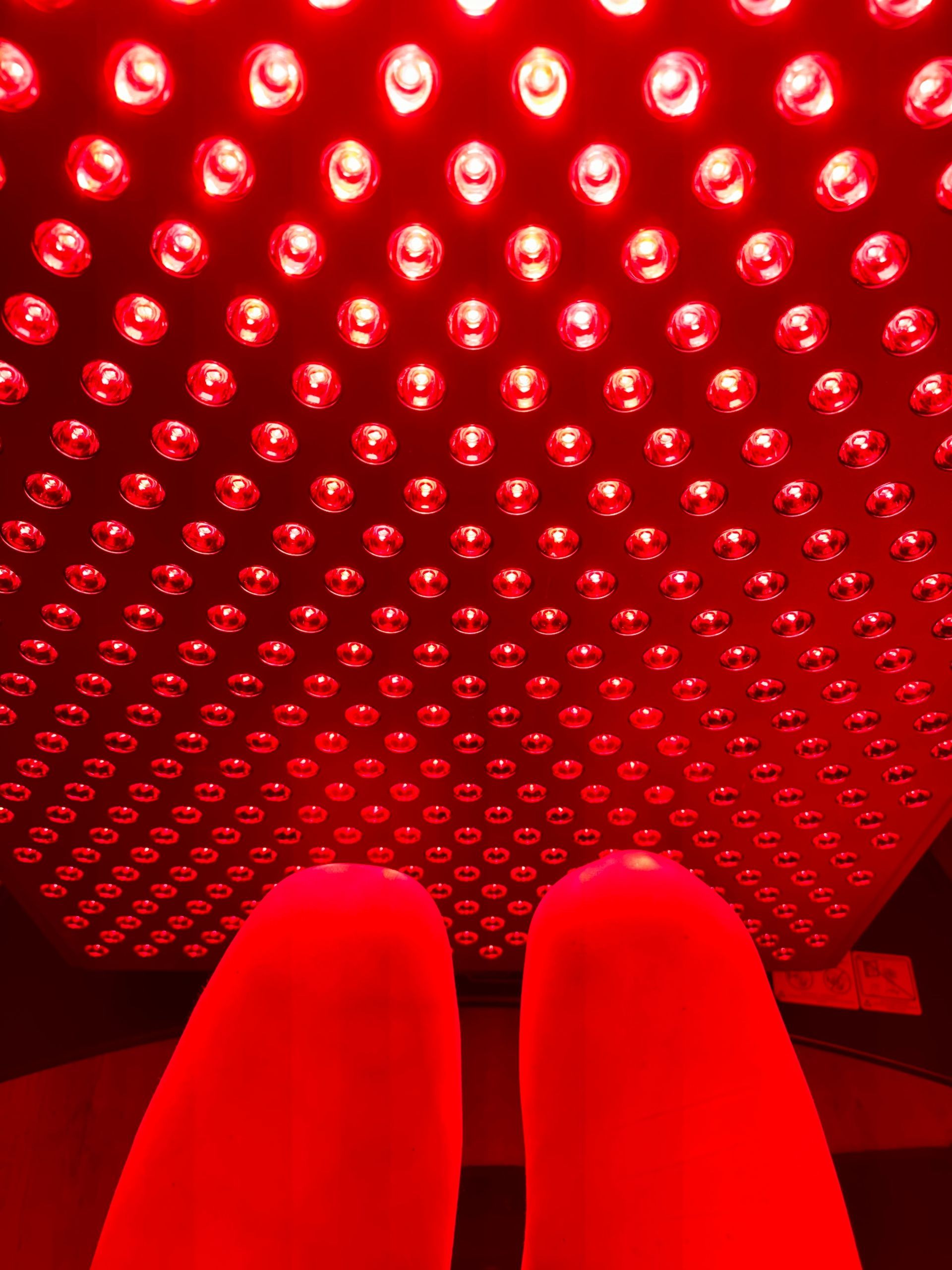 Feet under a red light therapy panel. Red light illuminates the feet and overhead panel.