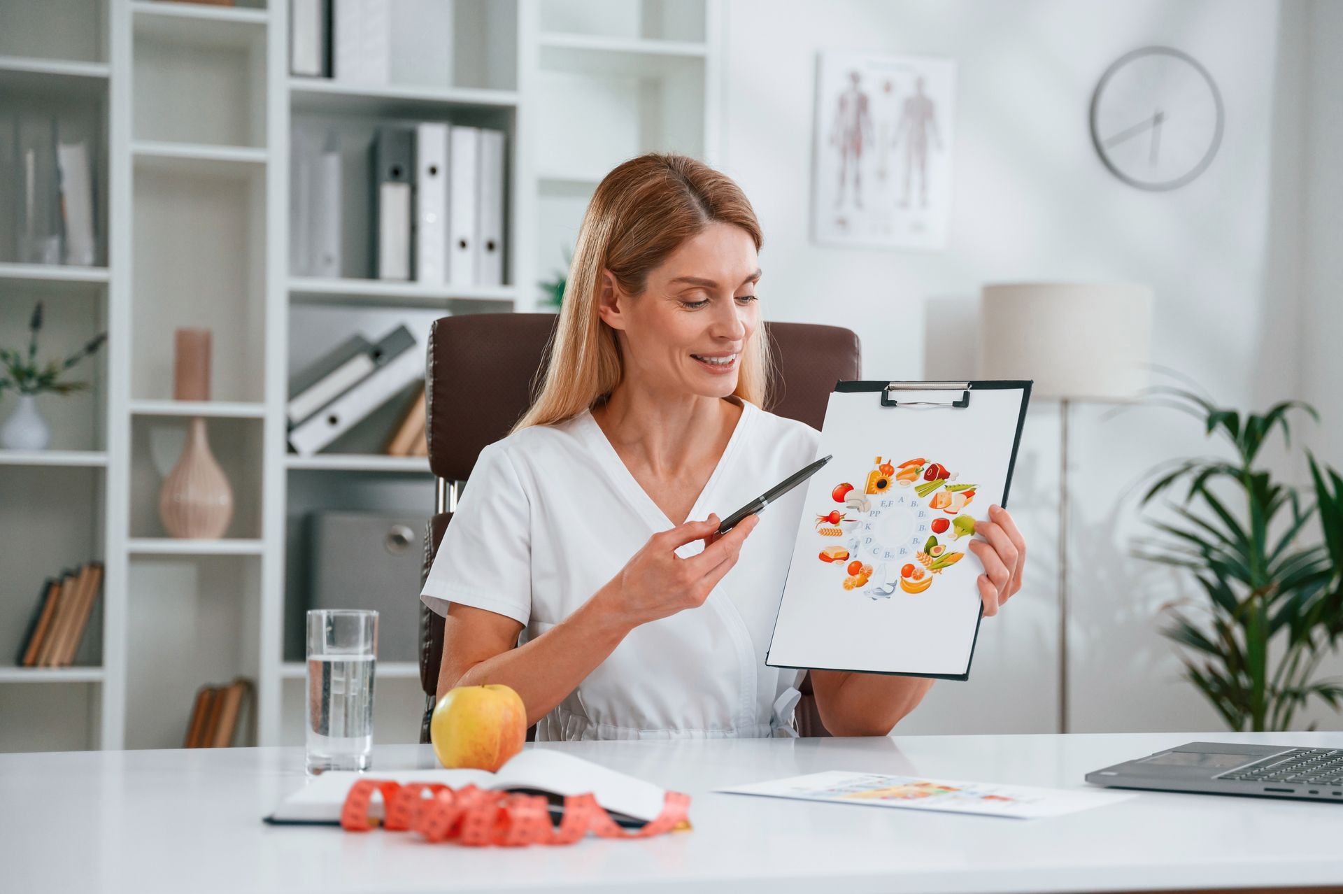 a woman is sitting at a desk holding a clipboard with a picture of fruits on it .