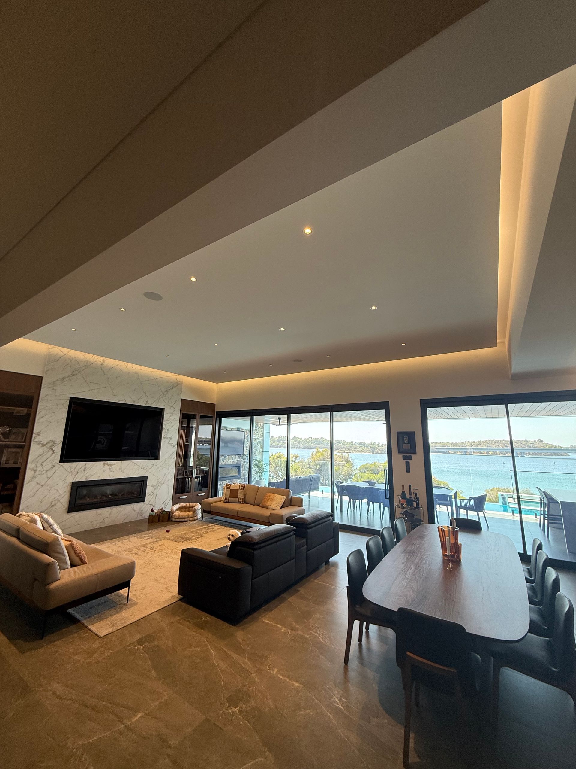 A man in a gray shirt and gloves drills drywall into a ceiling, working indoors.