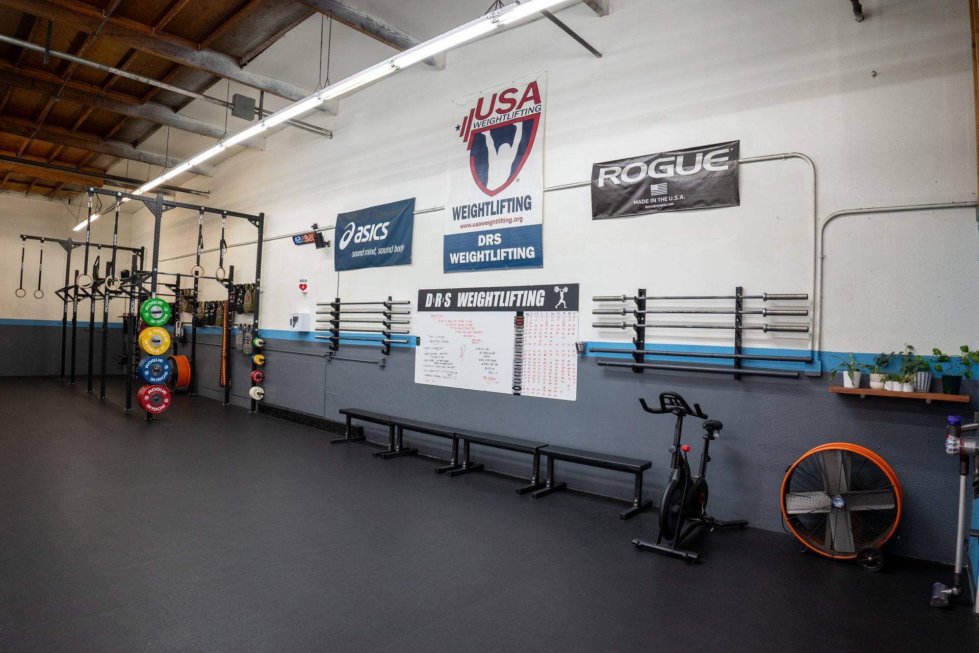 A gym with a lot of exercise equipment and a fan on the floor.