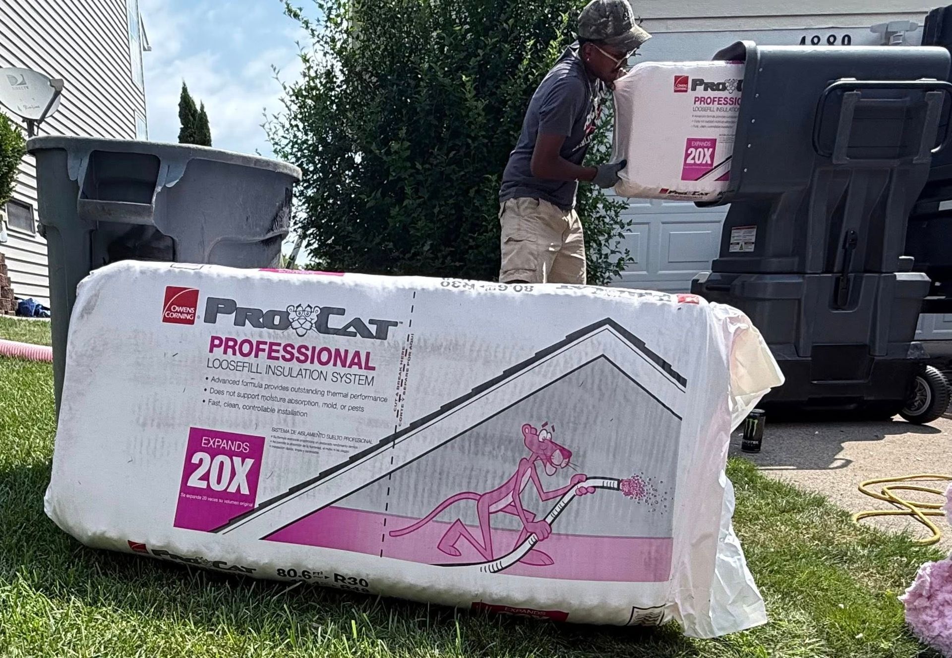 Person loading pink insulation from a bag into a machine outdoors near a trash can and a building.