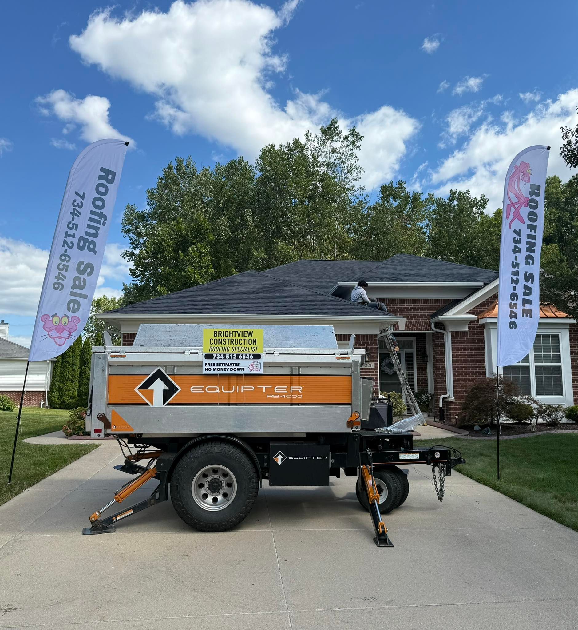 A roofing service trailer parked on a driveway in front of a house. White flags with logo.