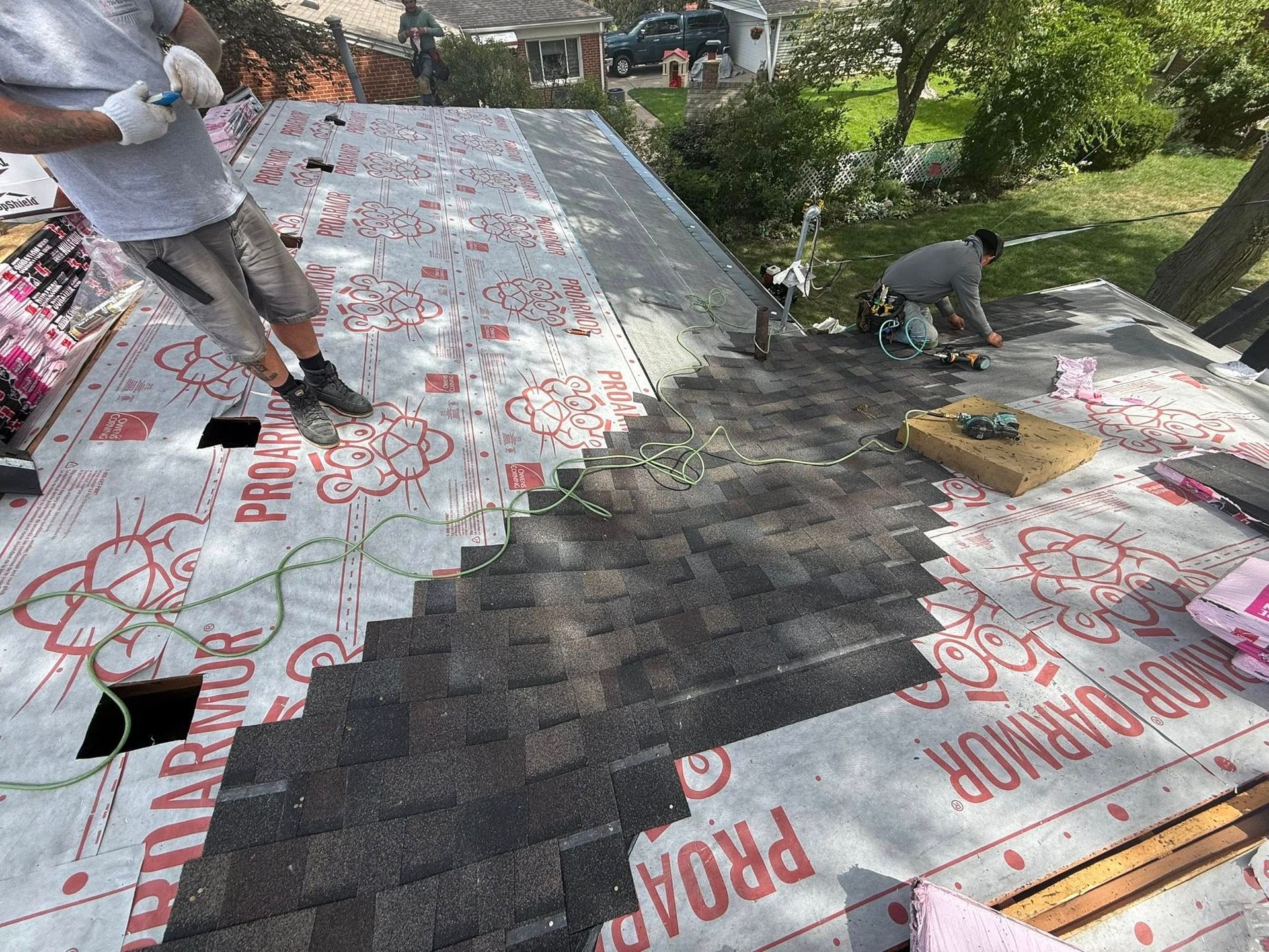 Roofers installing shingles on a house roof. One worker is standing, one is kneeling, covering the roof.