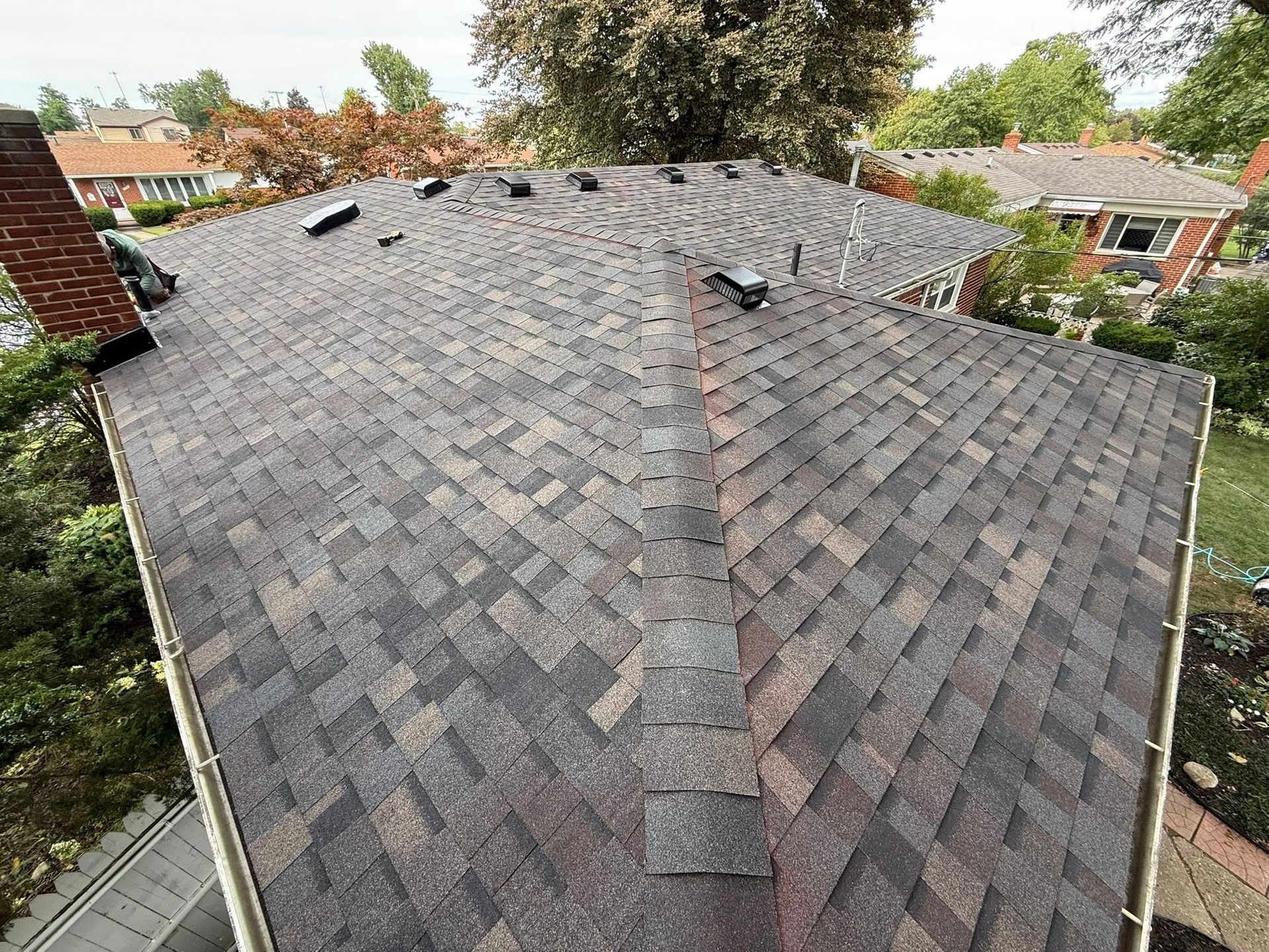 Dark brown asphalt shingle roof, with vents, on a residential house, viewed from above.