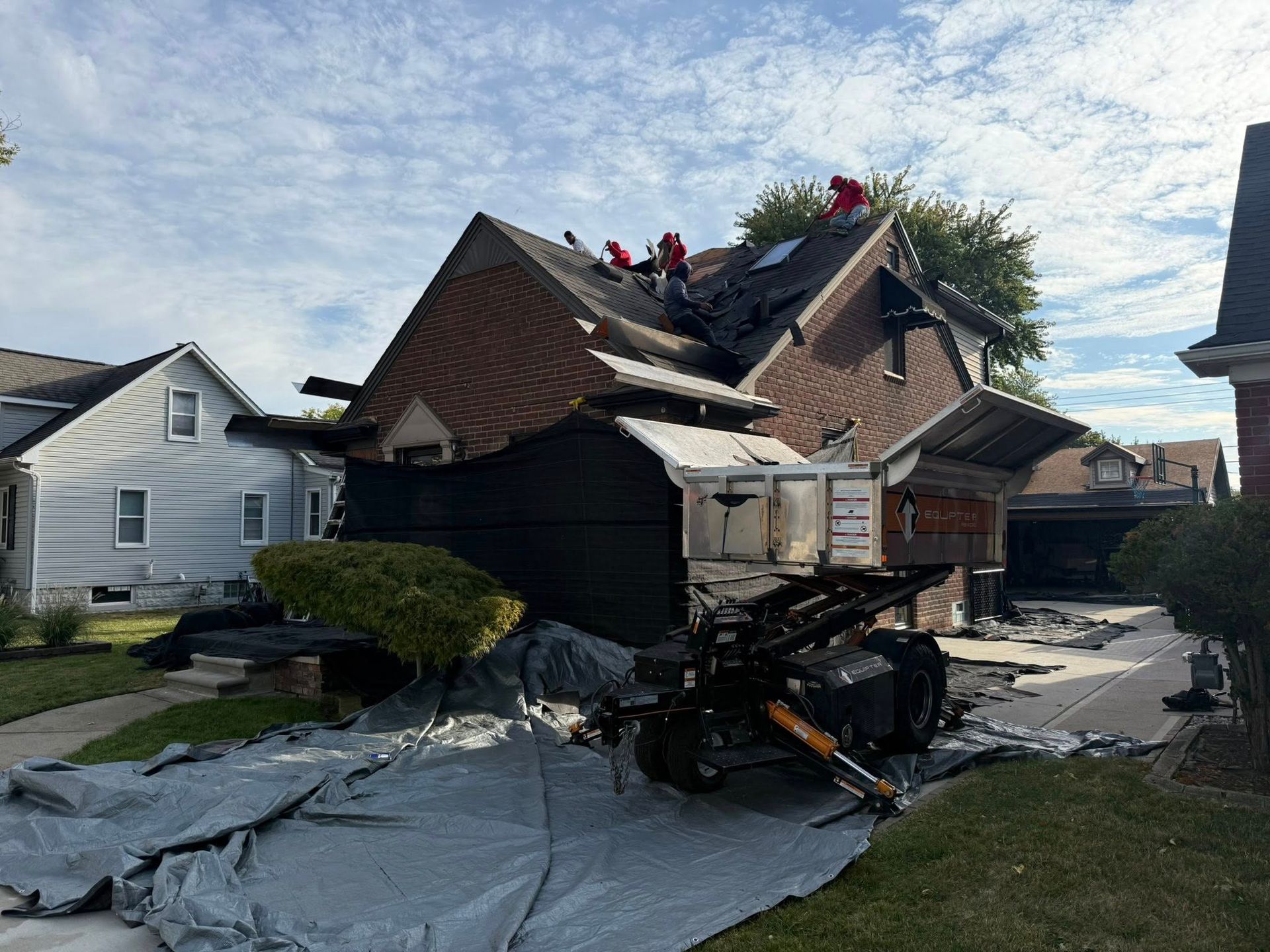Roofers working on damaged roof of a brick house. Debris and equipment visible on the ground.