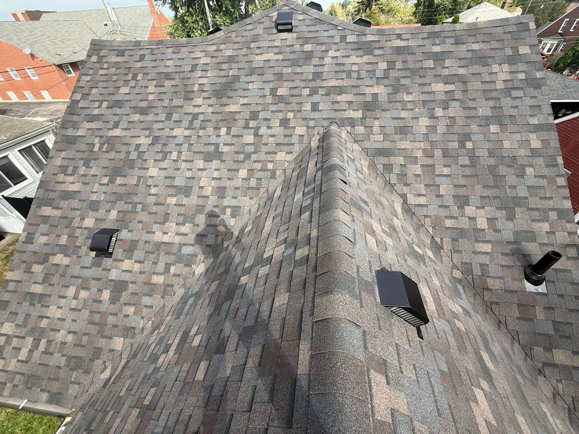 Overhead view of a house roof with brown and gray shingles, and several vents.
