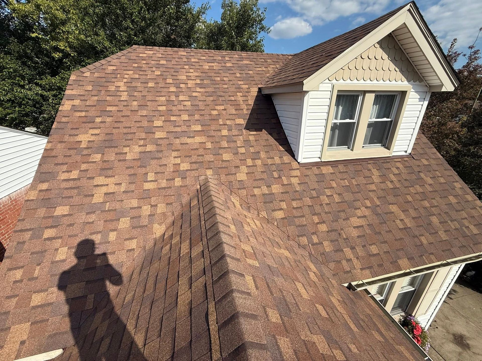 Brown shingled roof with a dormer window, under a blue sky.