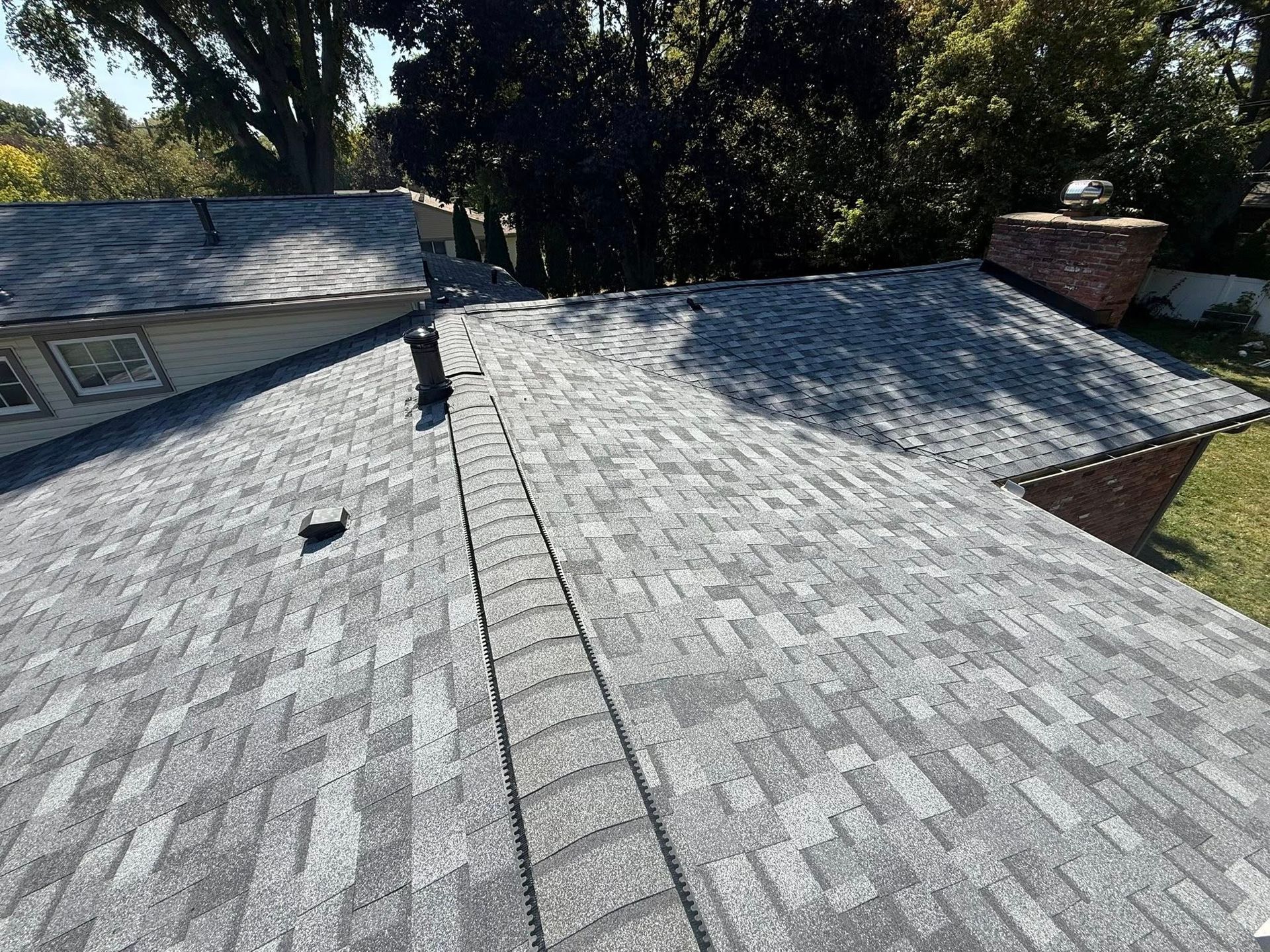 Gray asphalt shingle roof on a house, with a chimney and trees in the background.