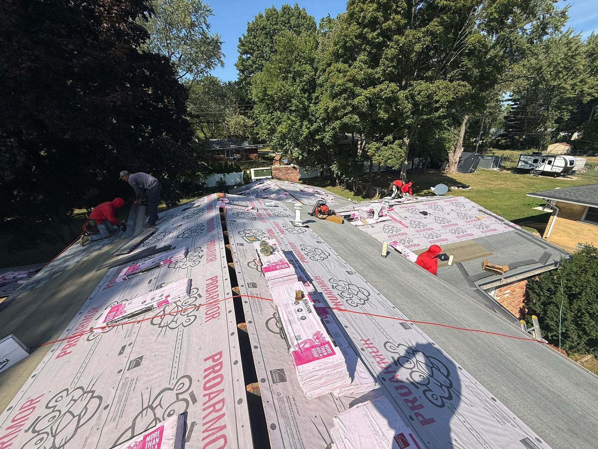 Roofers in red shirts installing new roofing material on a house, sunny day.