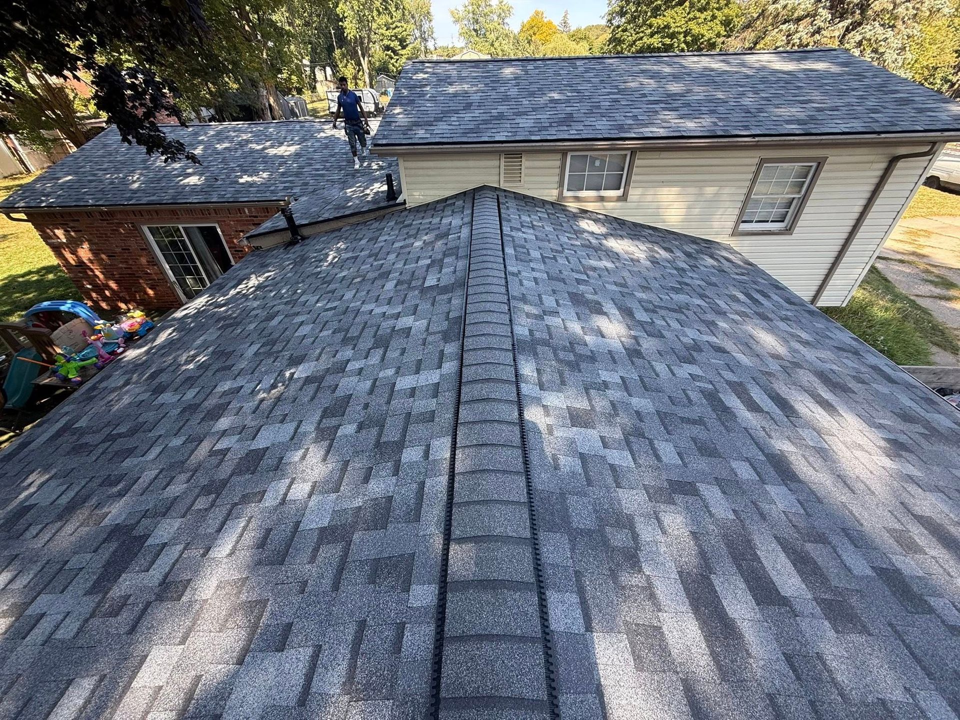 View from a roof of asphalt shingles. Two people stand on adjacent roofs.