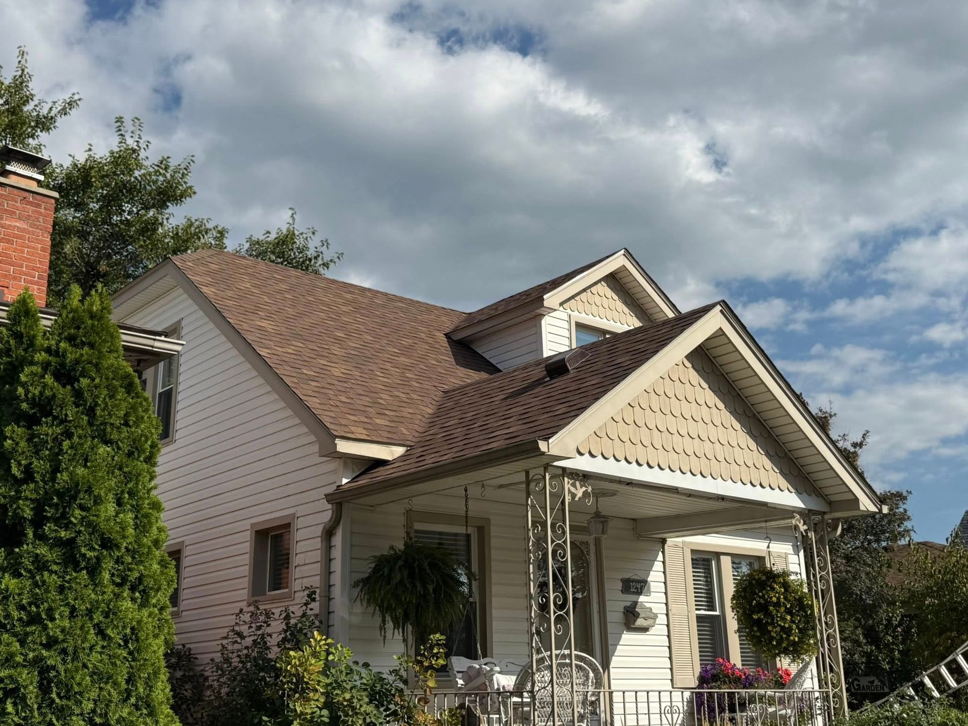 Two-story house with tan roof, white siding, small porch, and brick chimney under a cloudy sky.