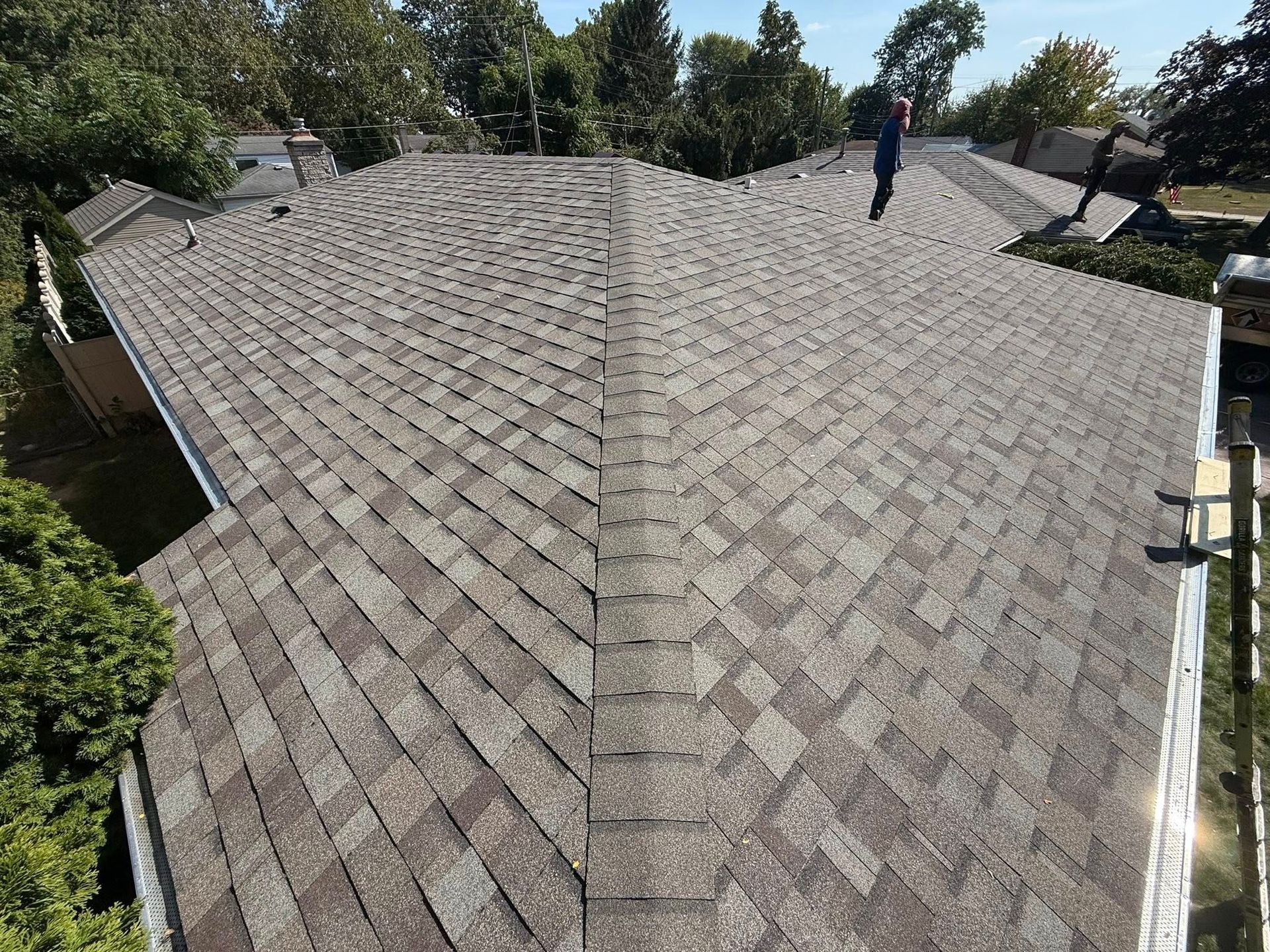 Overhead view of a house roof with gray asphalt shingles and a central ridge.