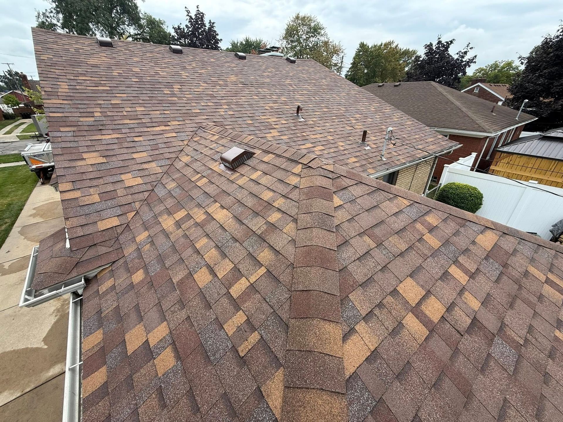 Brown and tan shingle roof with visible vents and gutters, on a cloudy day.