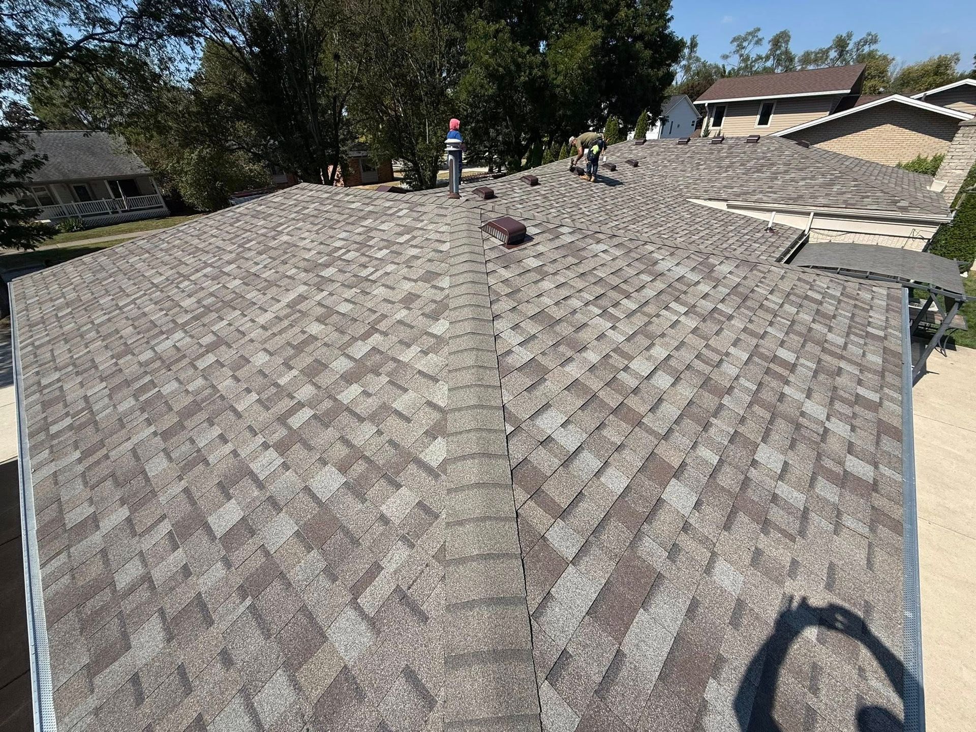 View of a brown shingle roof with a few workers.