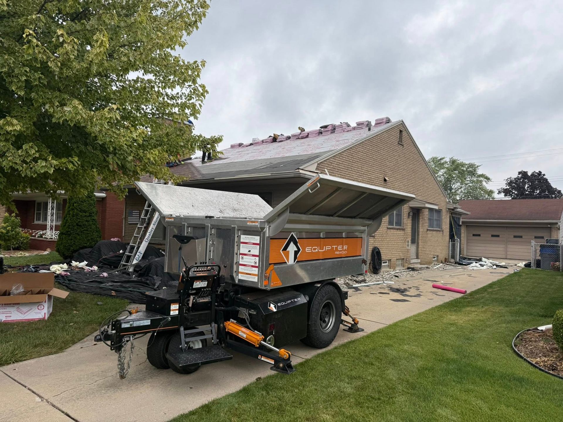 A trailer with roofing materials parked in front of a house under construction.
