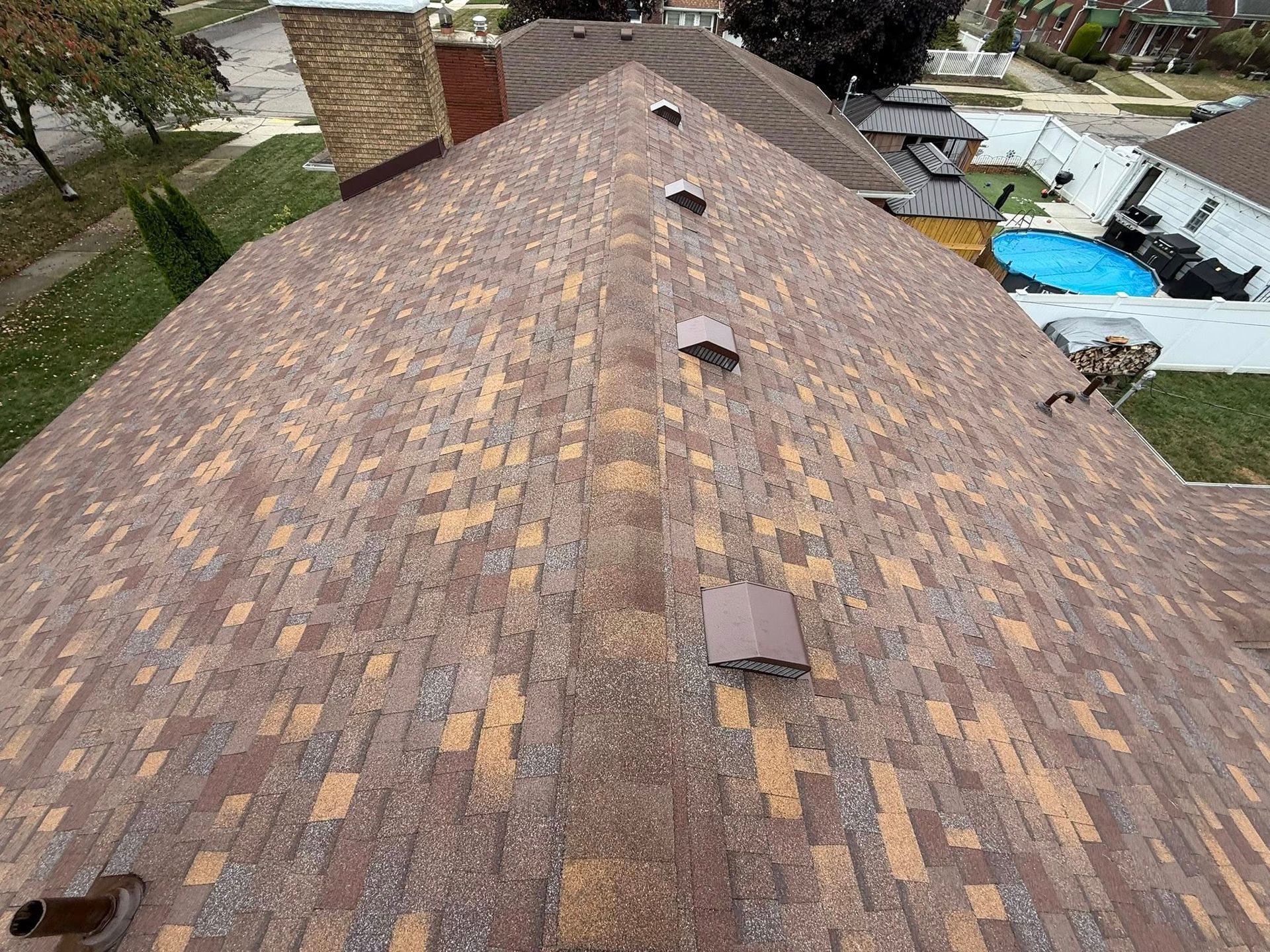 Brown shingled roof with multiple small vents and a brick chimney.