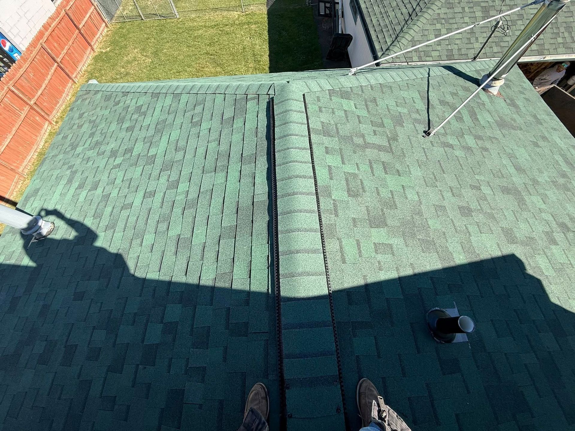 Overhead view of green shingled roof with person's feet visible, likely assessing or working.