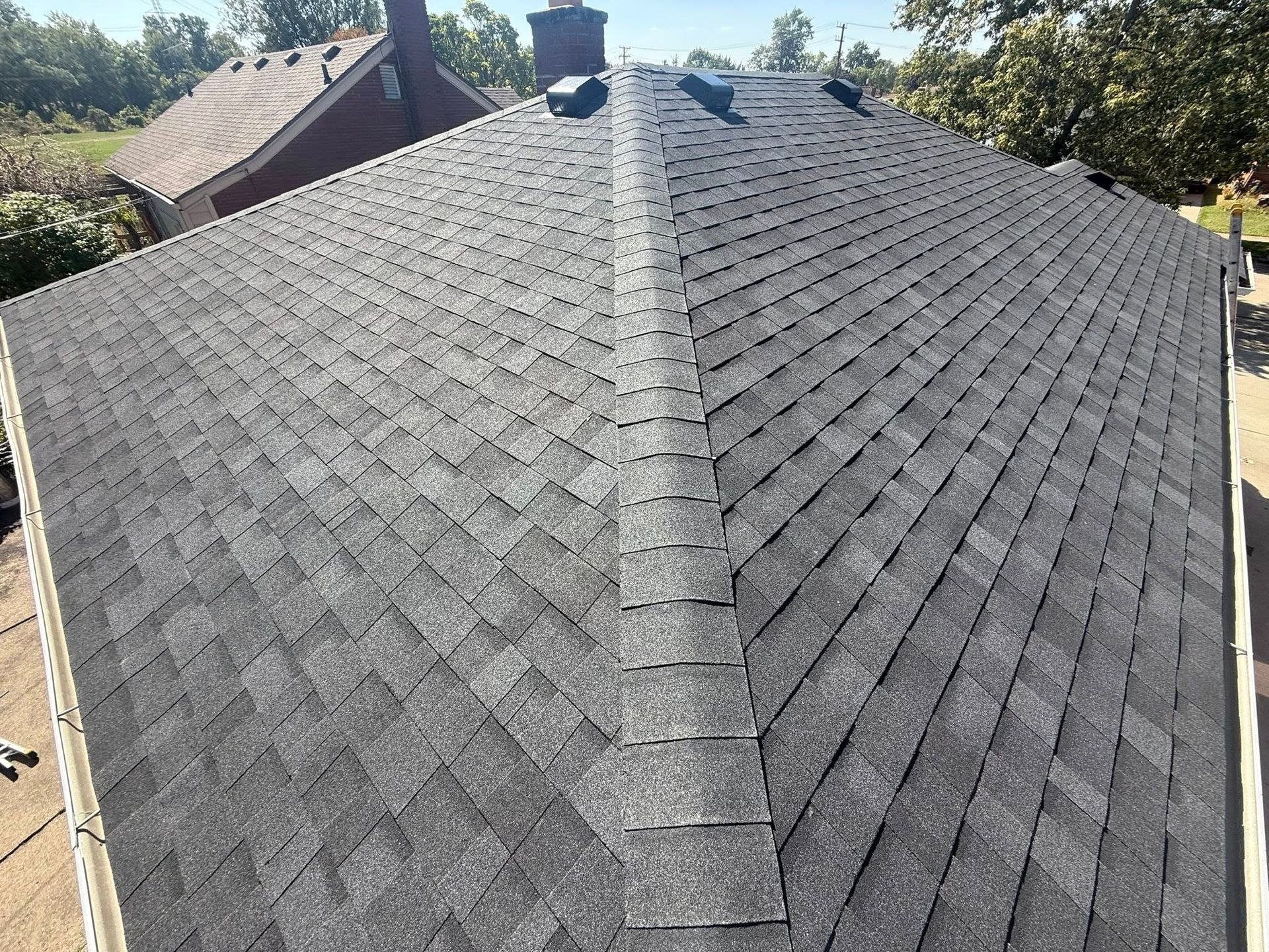 Newly shingled, gray asphalt roof on a home, viewed from above, with a central ridge.