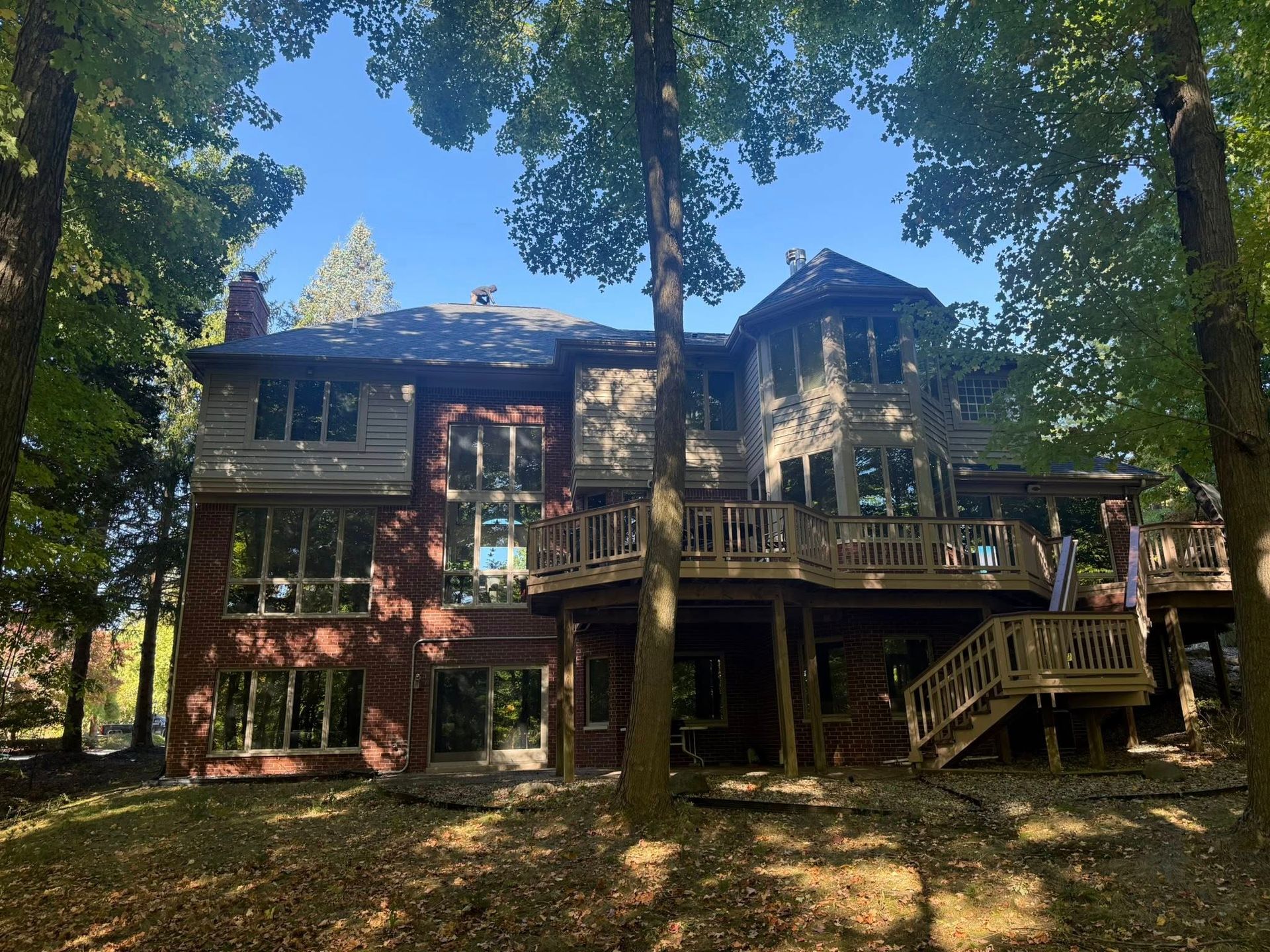 Two-story house with brick and wood siding, large windows, and a wooden deck, surrounded by trees.