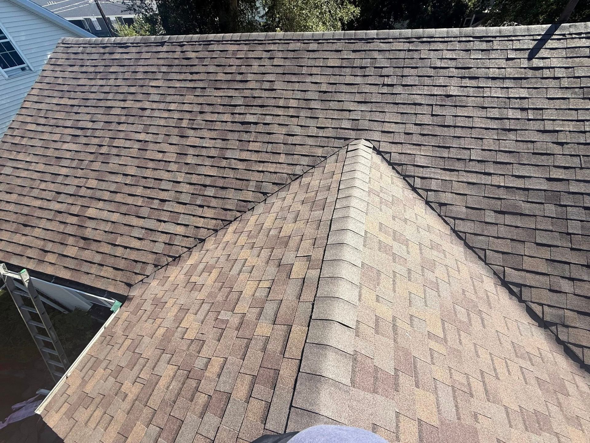 Overhead view of a shingled roof with a central triangular peak, displaying weathered brown tiles.