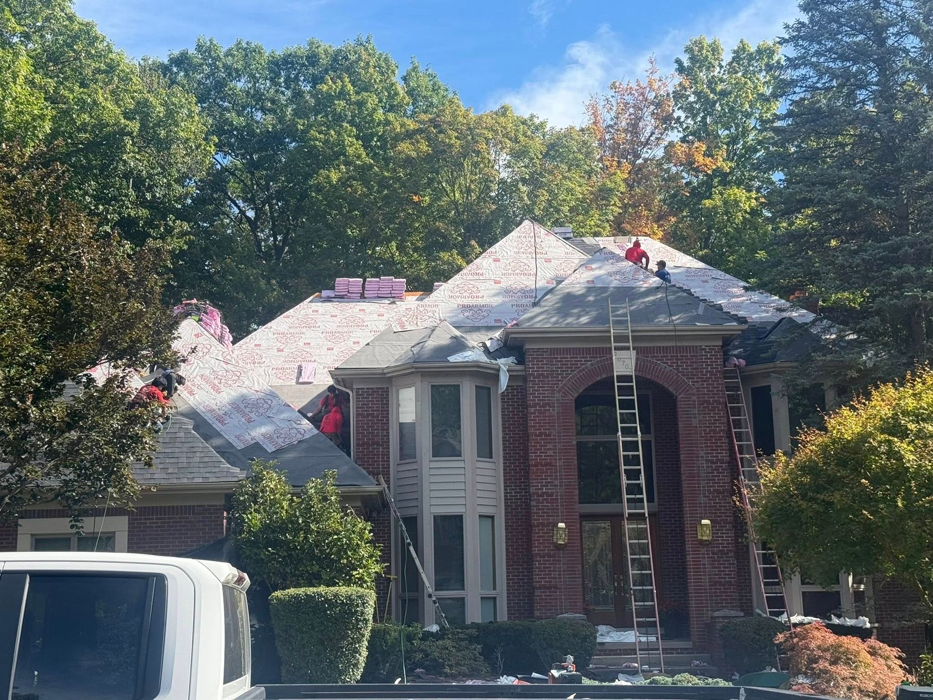 Roofers on a house with exposed underlayment; ladder propped against the brick facade.