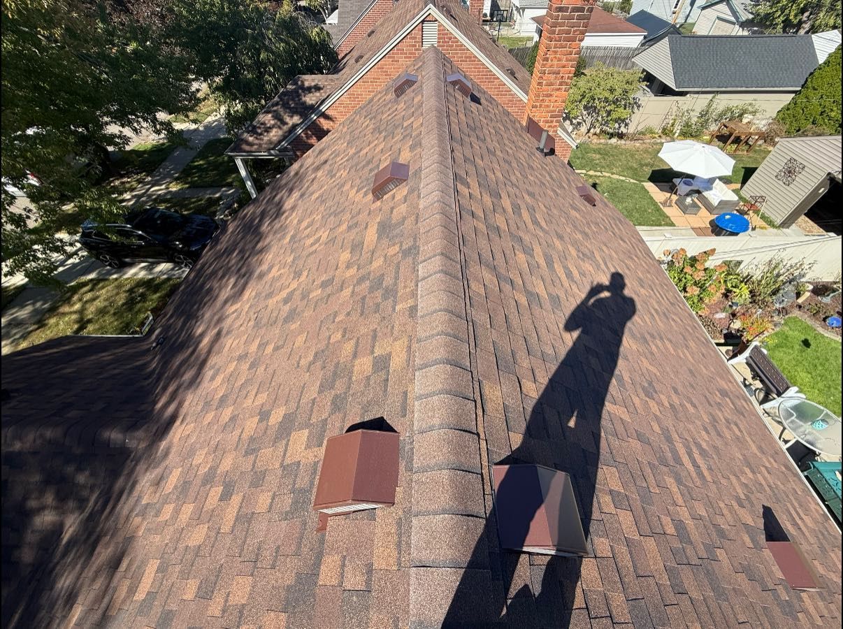View of a brown shingle roof with a person's shadow cast over it on a sunny day.
