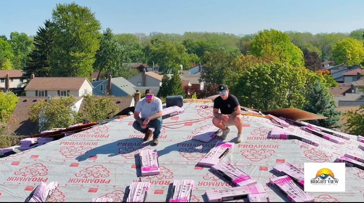 Two men on a rooftop with pink insulation and a sunny suburban backdrop.
