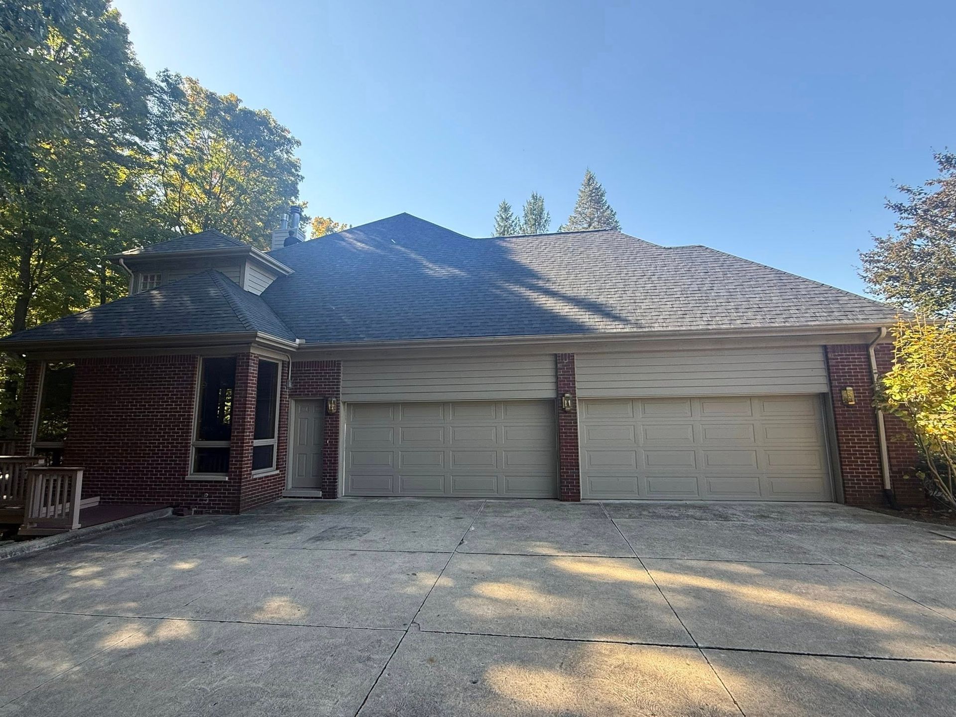 Brick house with two garage doors and a roof, on a concrete driveway, under a blue sky.
