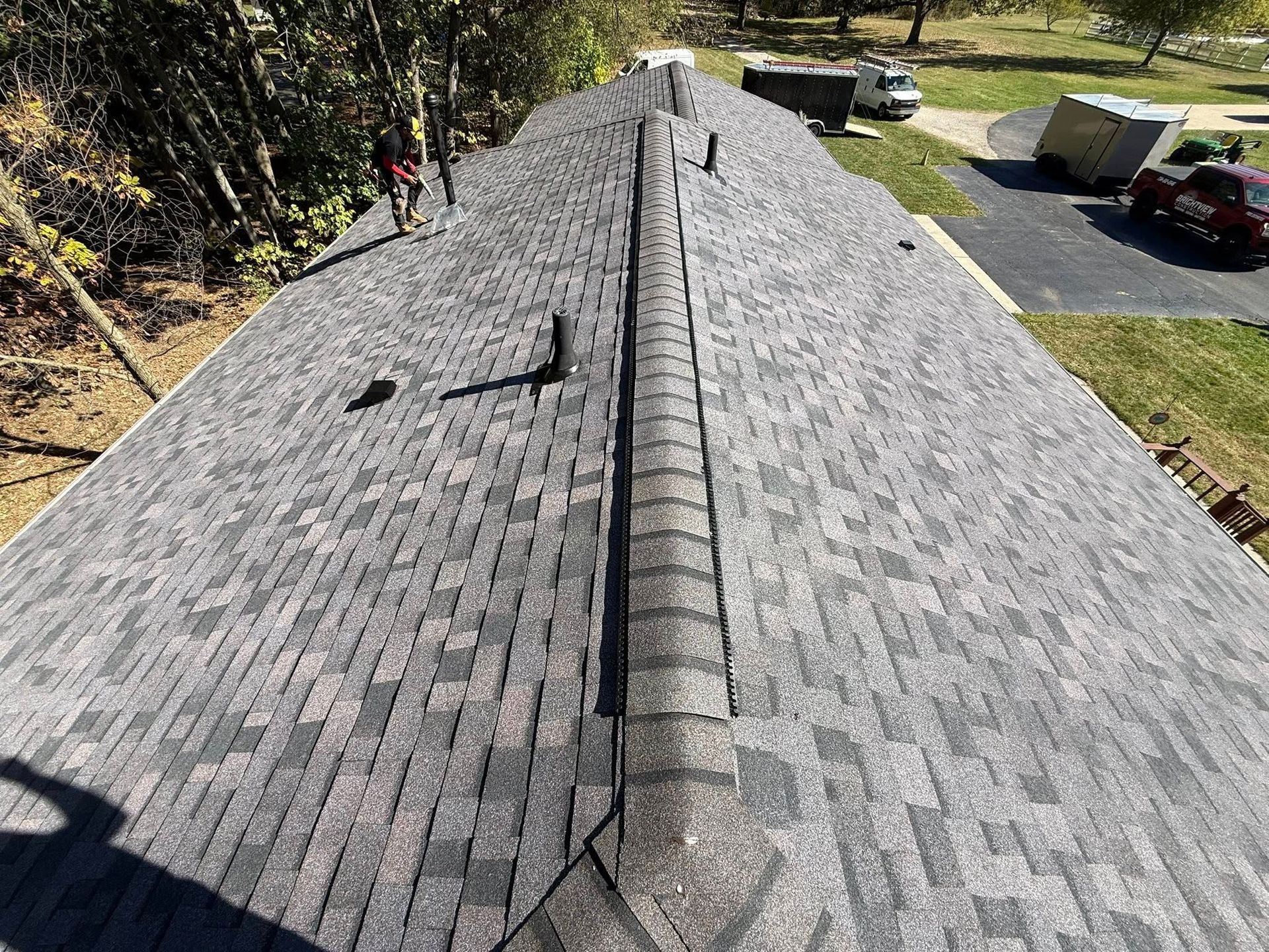 Newly shingled gray roof with a central ridge. Two people work on the roof.