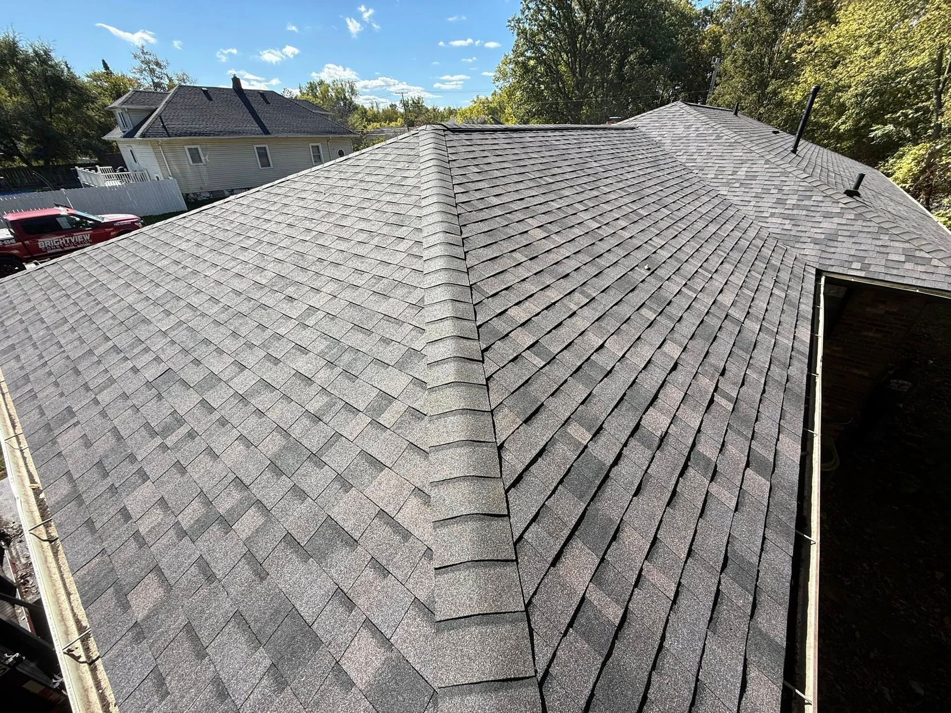 View of a residential roof with gray asphalt shingles under a blue sky.