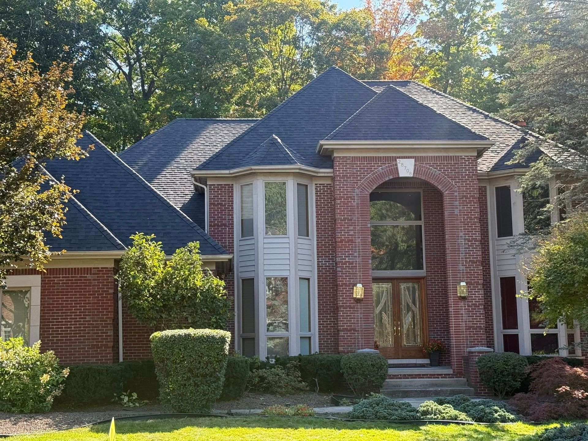 Red brick house with dark roof, arched doorway, and manicured landscaping.