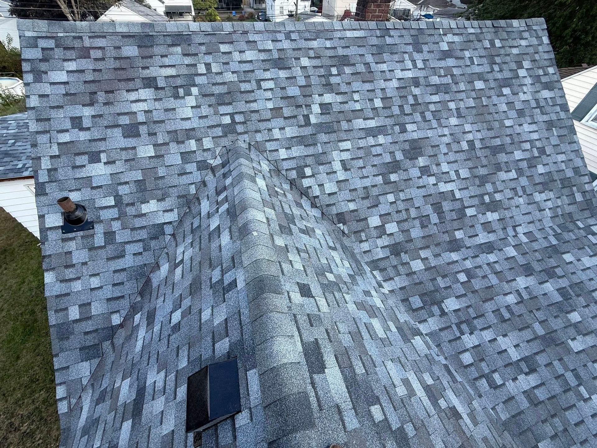 Gray asphalt shingle roof with a ridge, window, and chimney on a house.