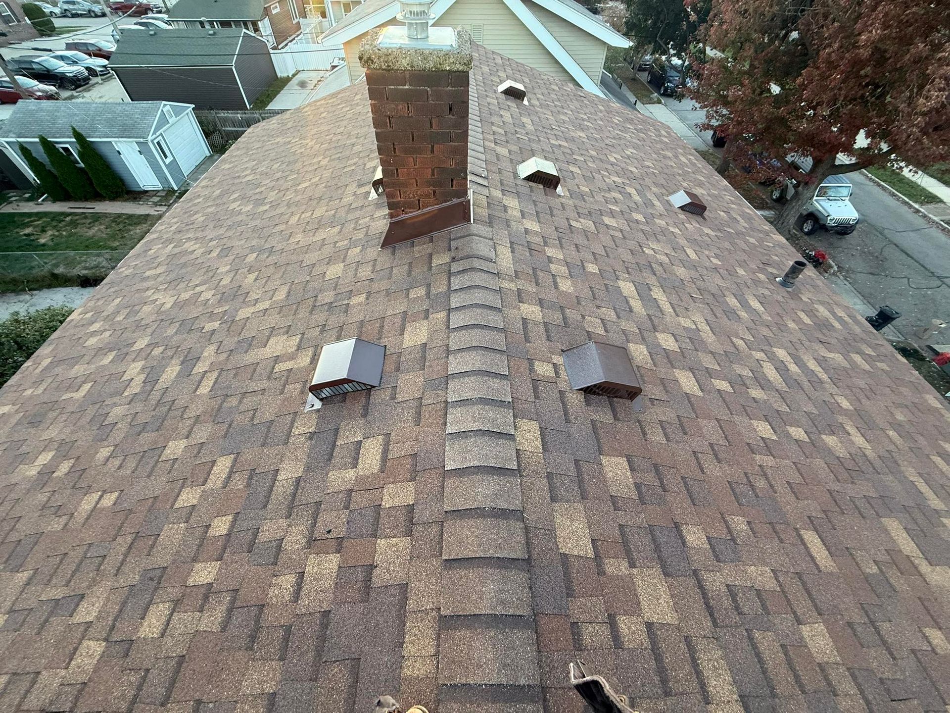 Brown asphalt shingle roof with a brick chimney and several vents. View from above.