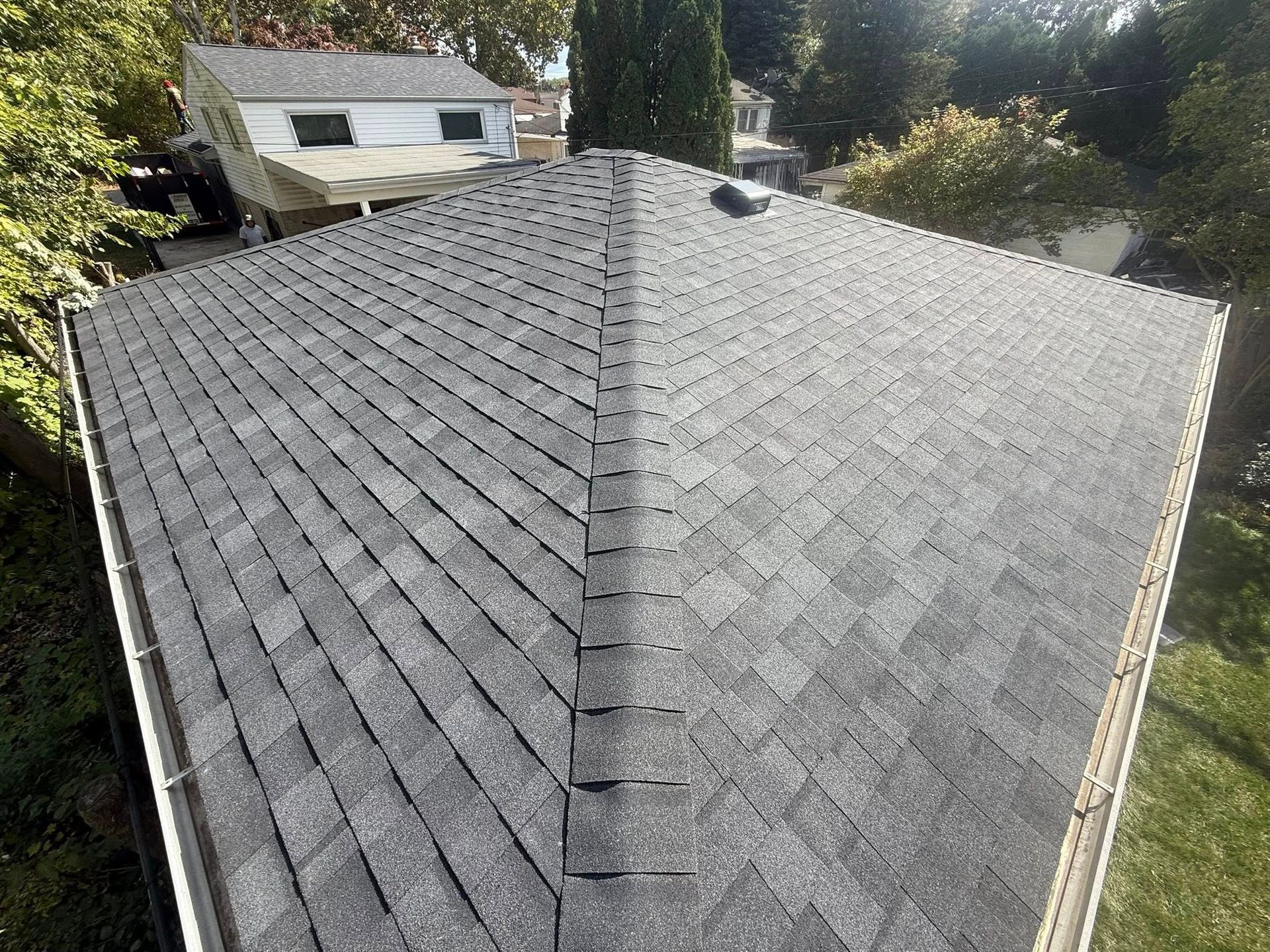 Gray asphalt shingle roof, close up. The roof has a peak and is surrounded by trees.
