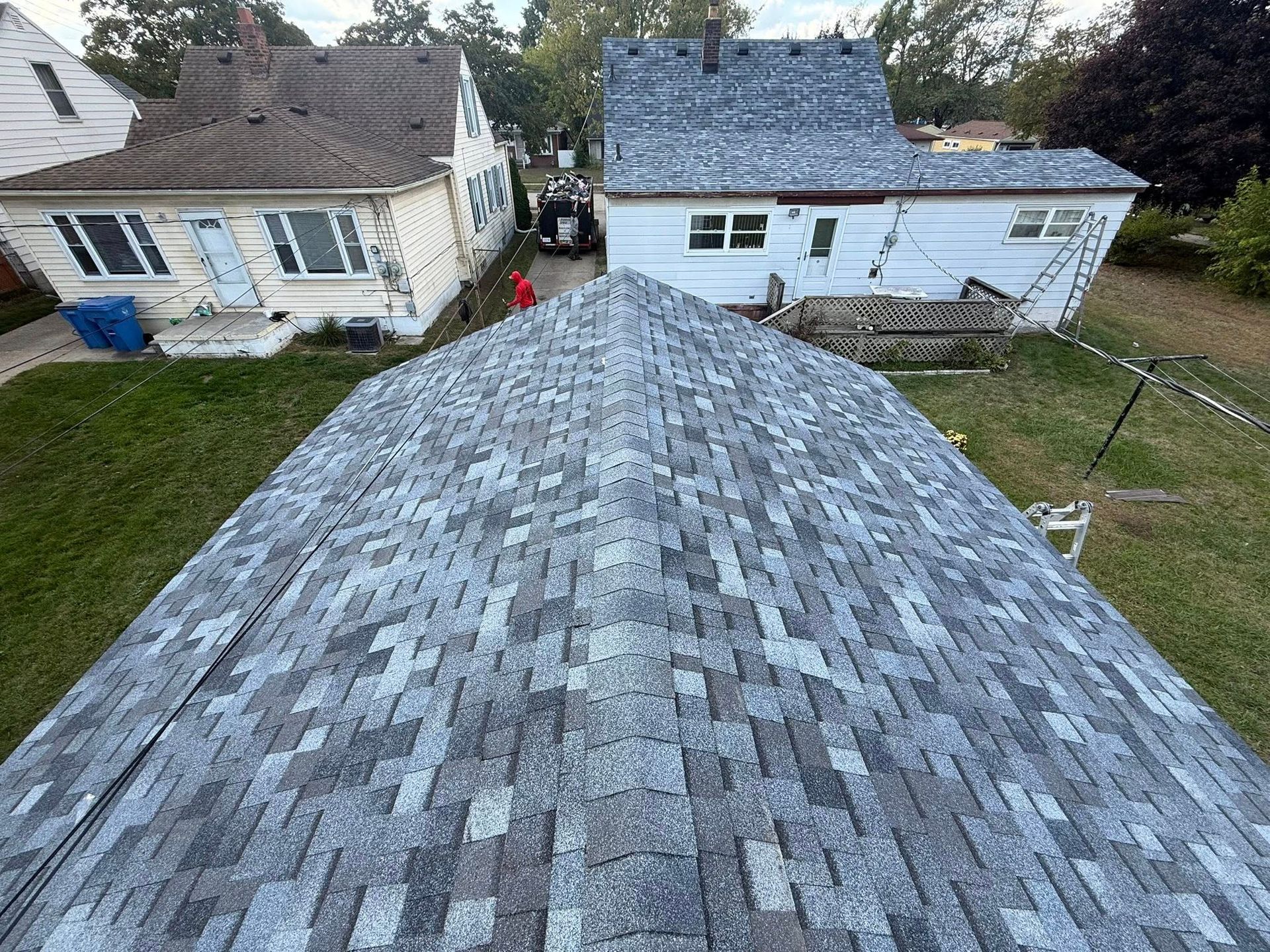 Overhead view of a house roof with grey shingles, backyard, and neighboring houses with green lawns.