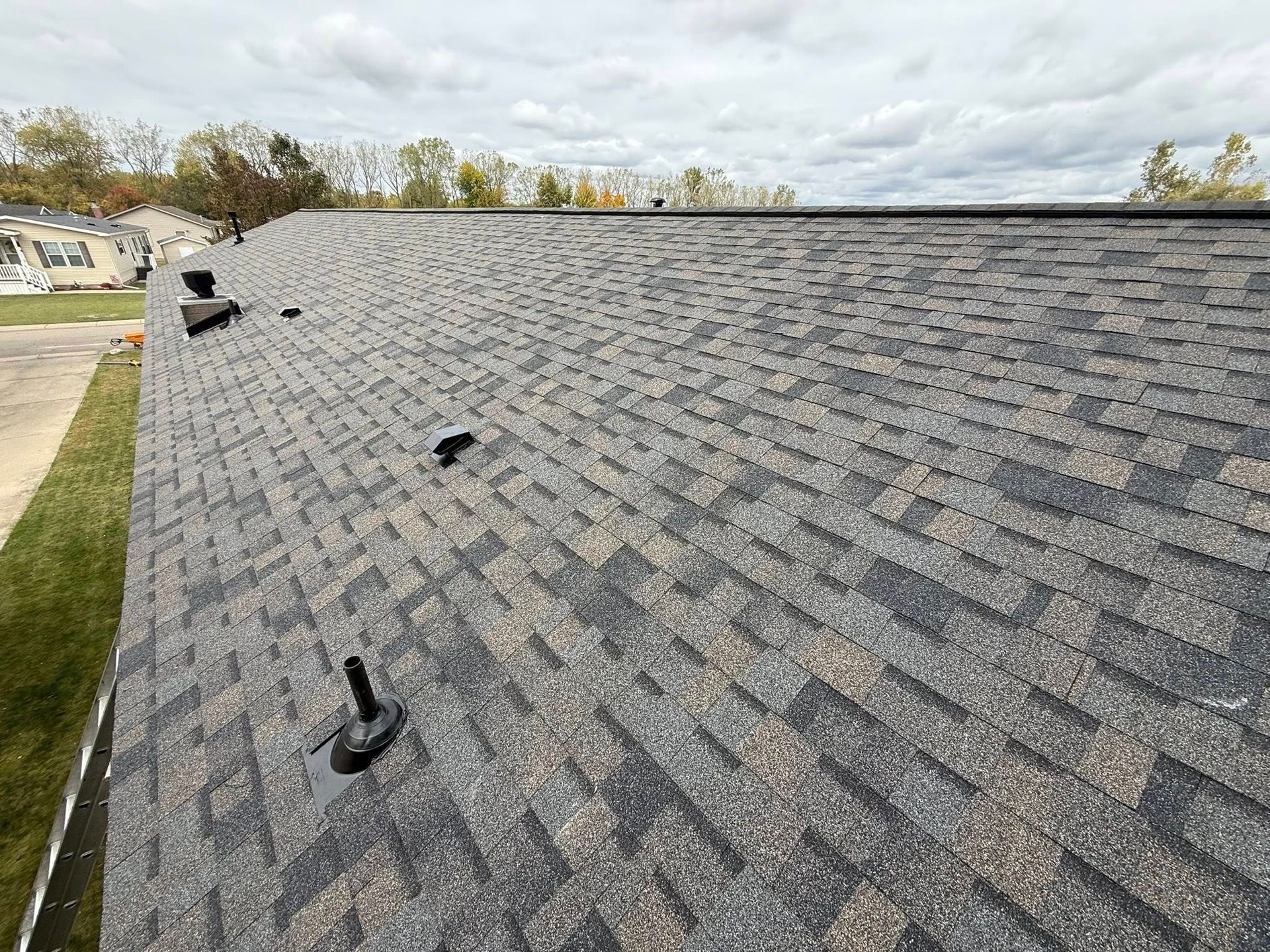 Close-up view of a dark brown asphalt shingle roof under a cloudy sky.
