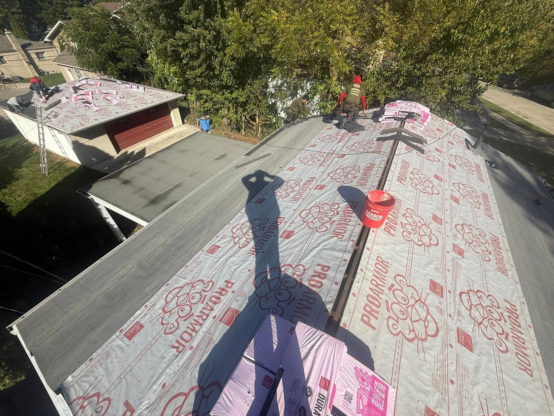 Roofer on a house roof installing underlayment. Bright sunlight, residential setting, visible shadow.