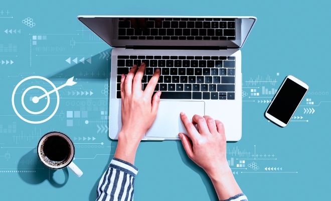 A person is typing on a laptop computer next to a cup of coffee and a cell phone.