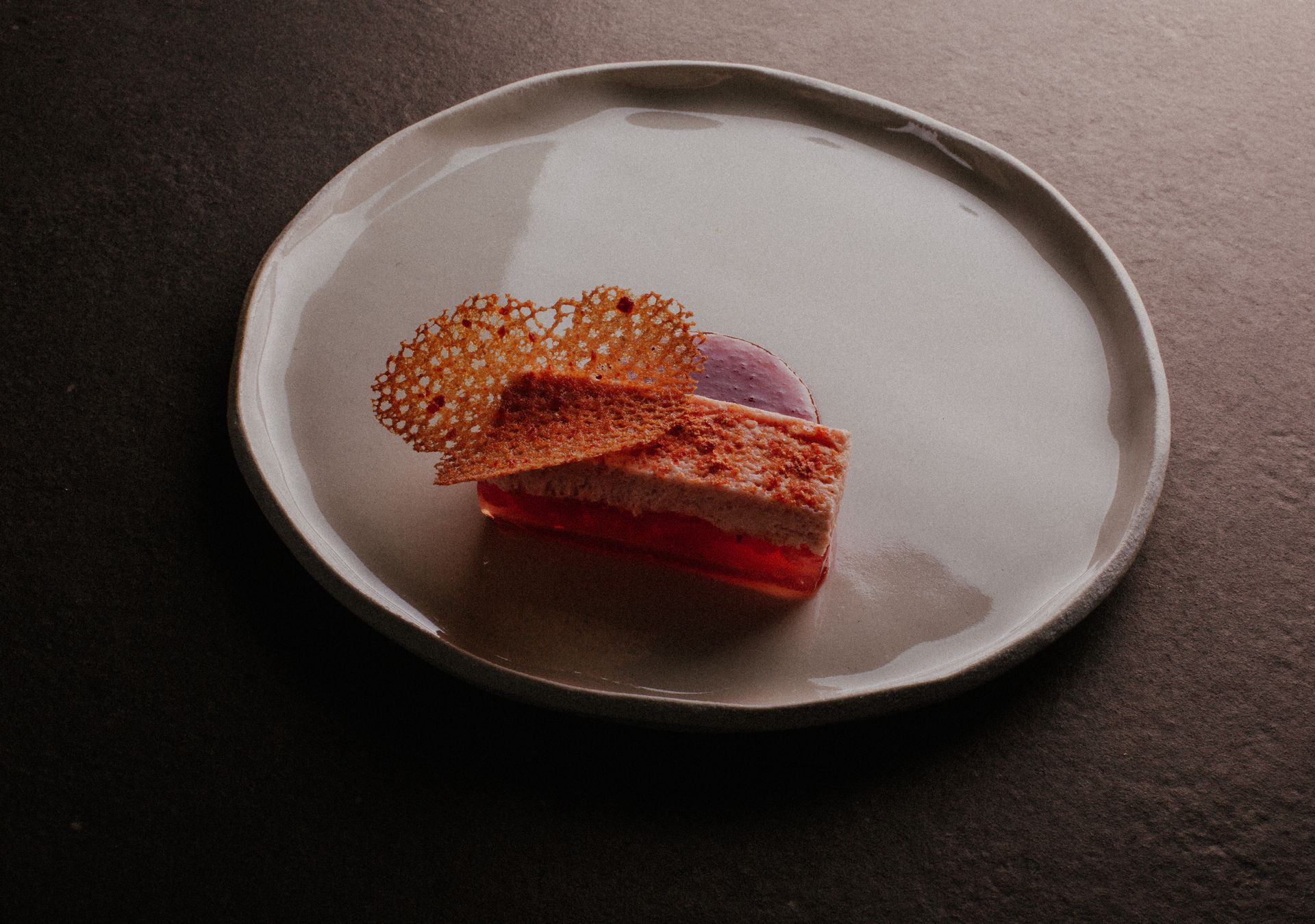 Assiette à dessert composée de couches de pâte feuilletée, de gelée, de tourbillon violet et d'un croustillant en forme de dentelle.