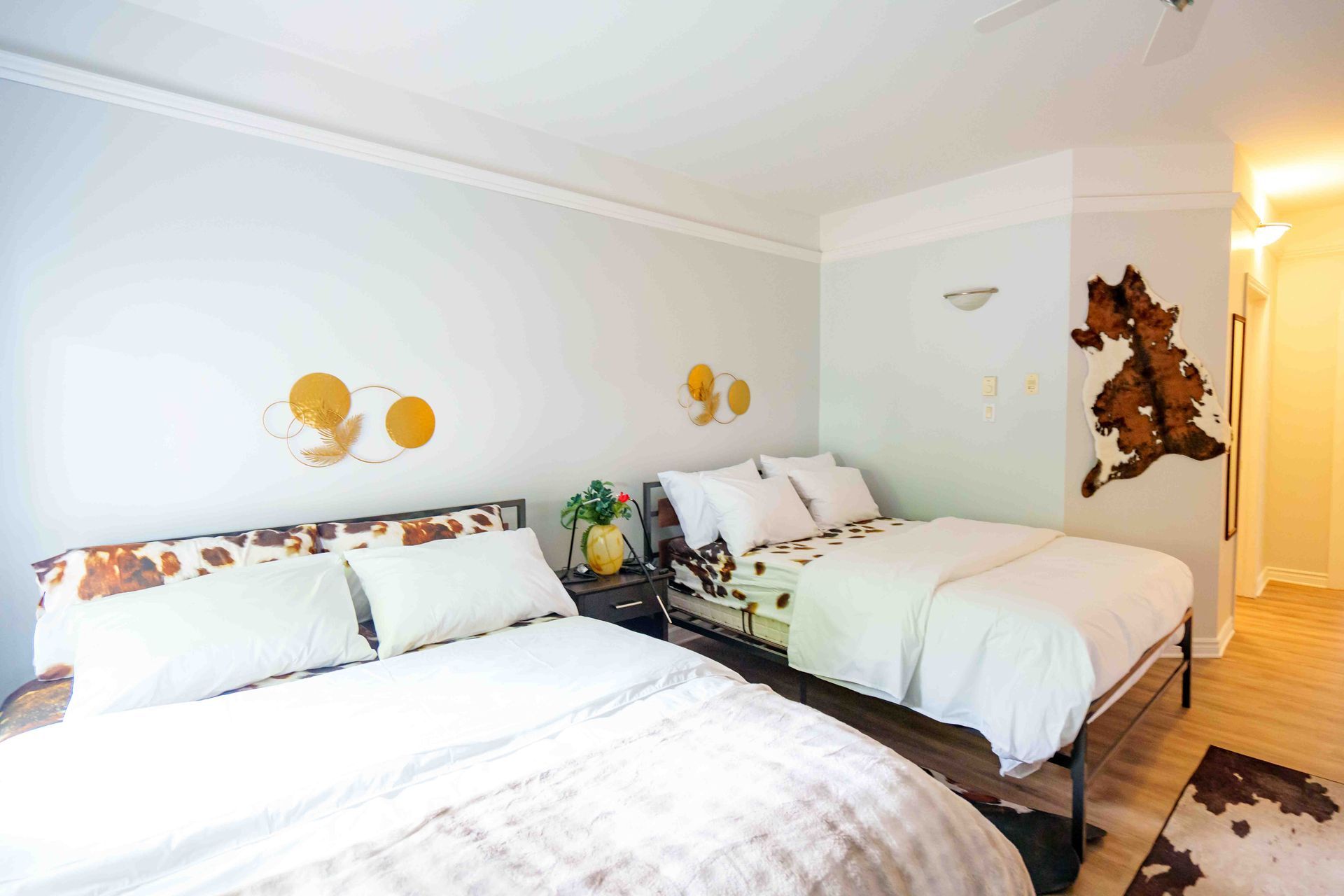 Deux lits avec des draps blancs dans une chambre aux tons clairs. La décoration murale comprend des cercles dorés et une forme de peau de vache brune.