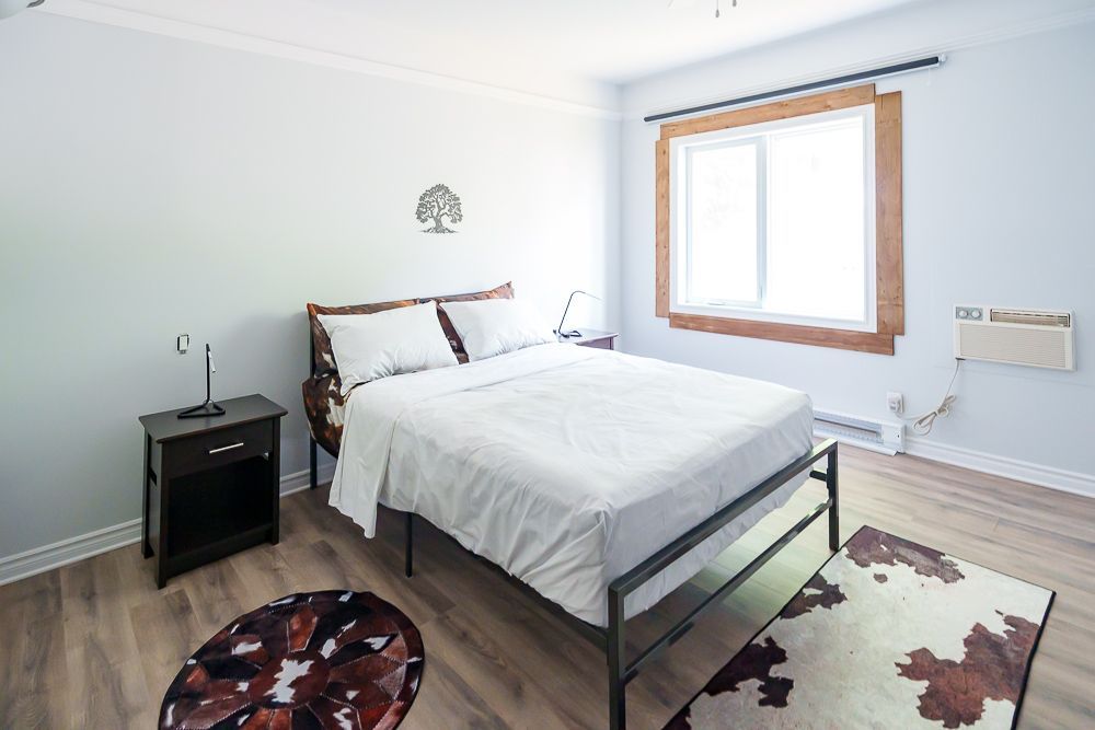 Chambre avec un lit, une table de chevet, des tapis et une fenêtre à cadre en bois.