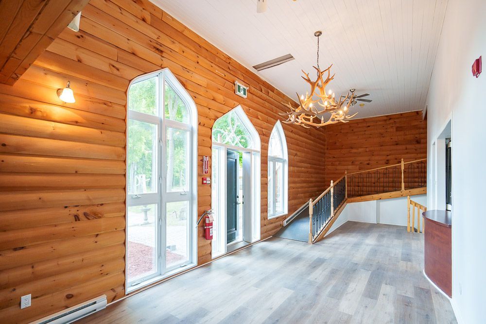Intérieur aux murs en bois avec fenêtres cintrées, lustre et escalier menant à l'étage.